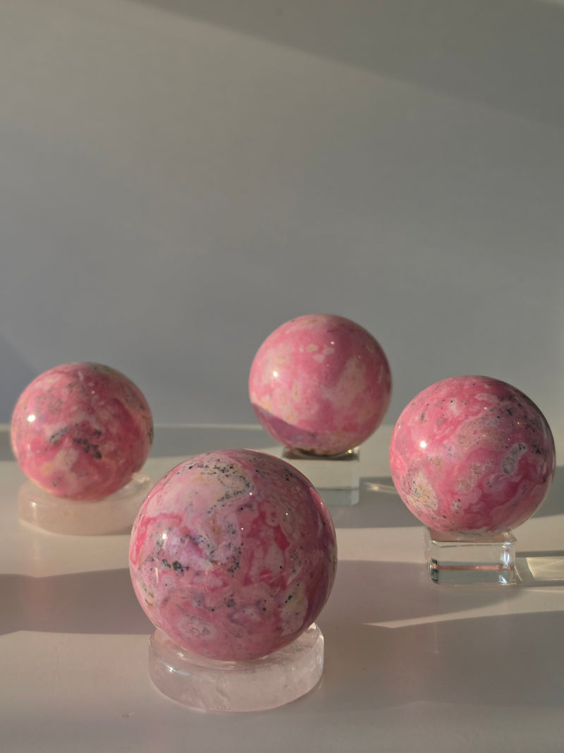 High quality Peruvian Pink Rhodonite crystal sphere with rich pink mineral patterns and elegant statement décor styling curated by Stone and Bloom.