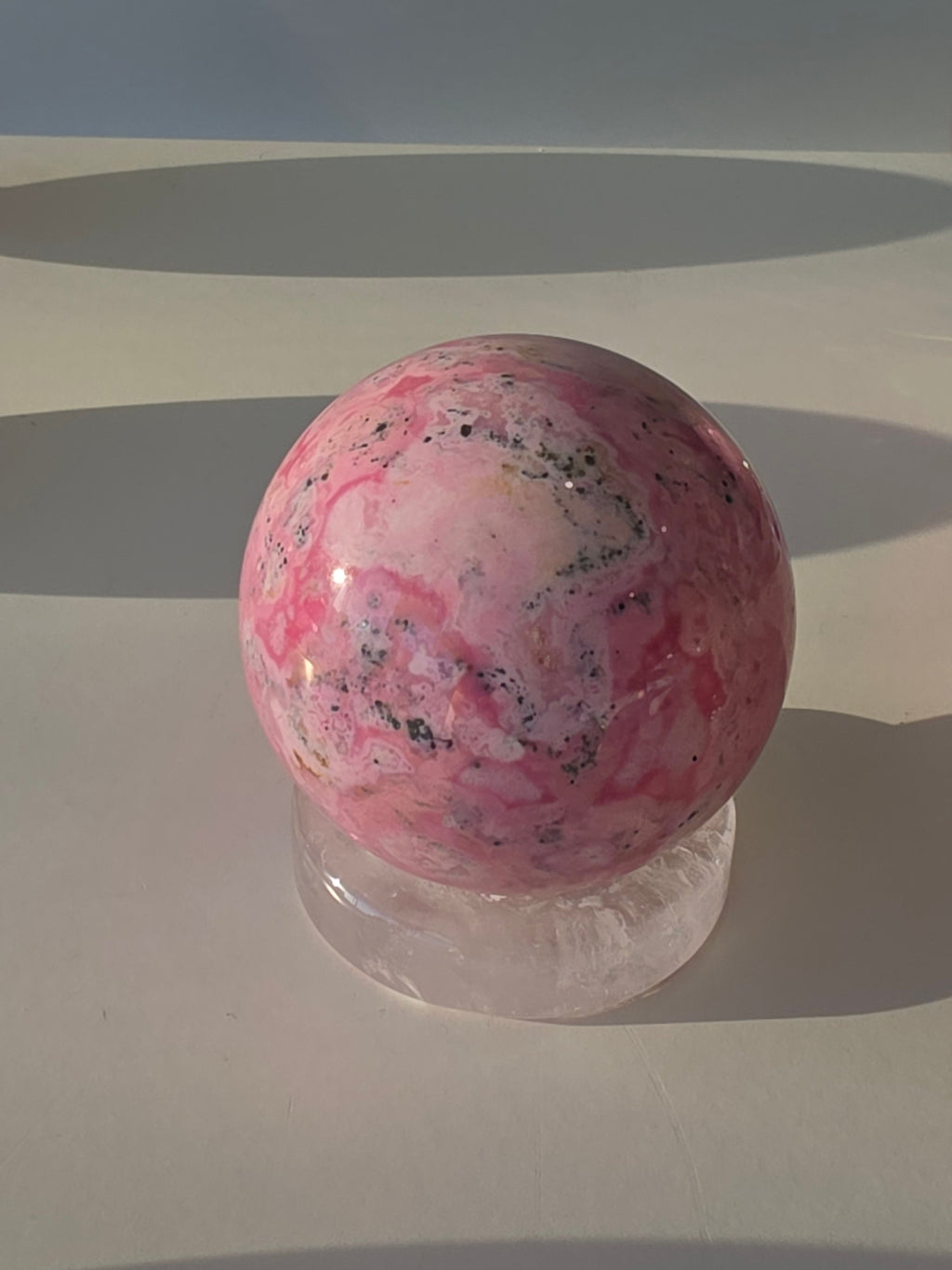 High quality Peruvian Pink Rhodonite crystal sphere with rich pink mineral patterns and elegant statement décor styling curated by Stone and Bloom.