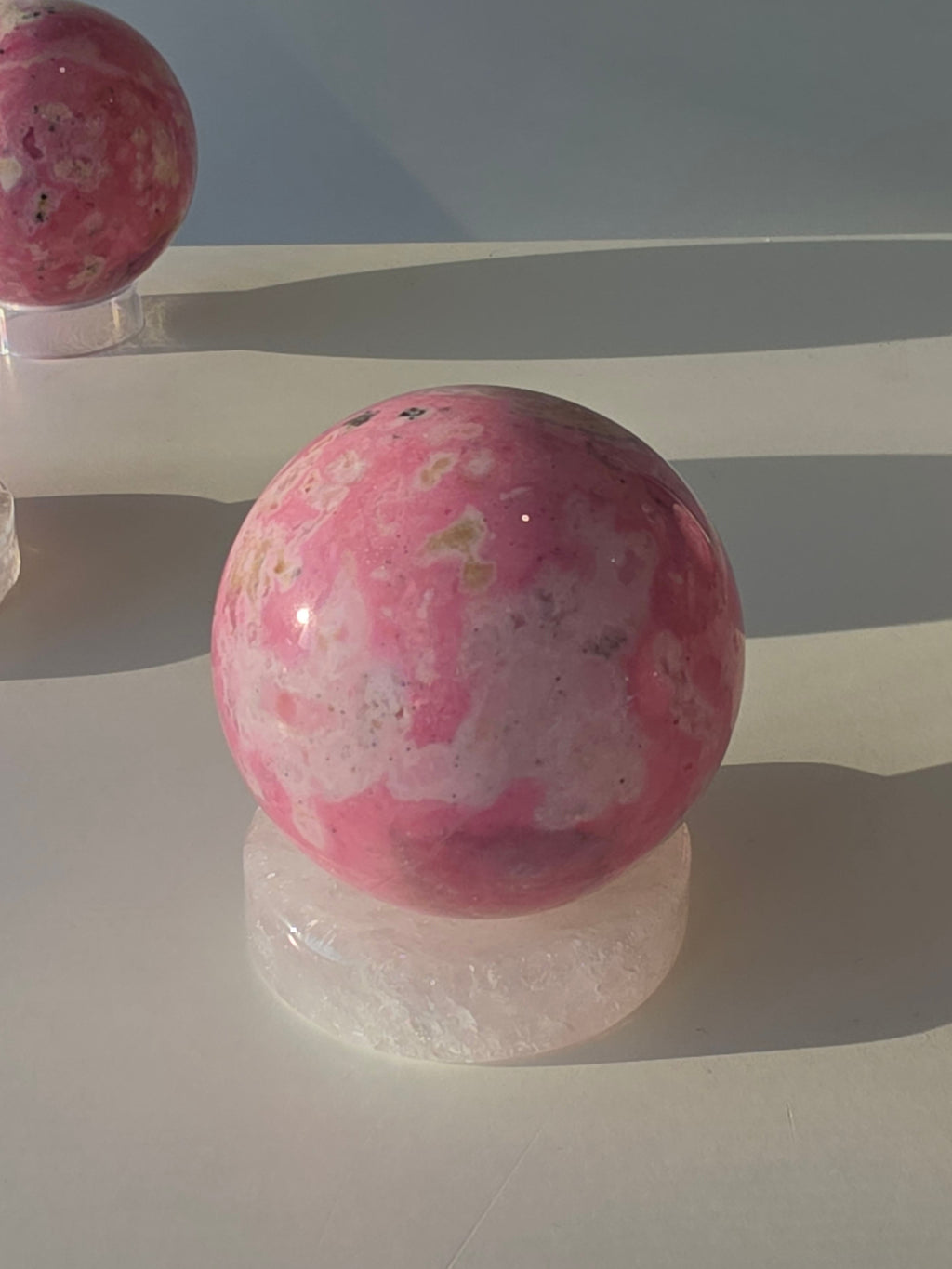 High quality Peruvian Pink Rhodonite crystal sphere with rich pink mineral patterns and elegant statement décor styling curated by Stone and Bloom.