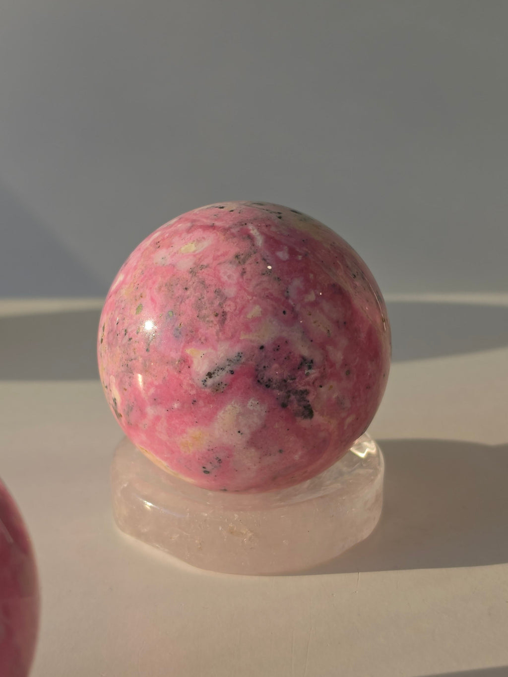 High quality Peruvian Pink Rhodonite crystal sphere with rich pink mineral patterns and elegant statement décor styling curated by Stone and Bloom.