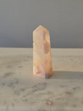 High-grade Pink Amethyst crystal tower featuring soft blush pink tones, sparkling druzy crystal formations, natural crystalline pockets, and polished geometric facets, photographed in natural light.