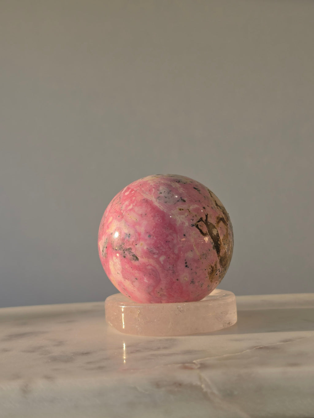 High quality Peruvian Pink Rhodonite crystal sphere with rich pink mineral patterns and elegant statement décor styling curated by Stone and Bloom.
