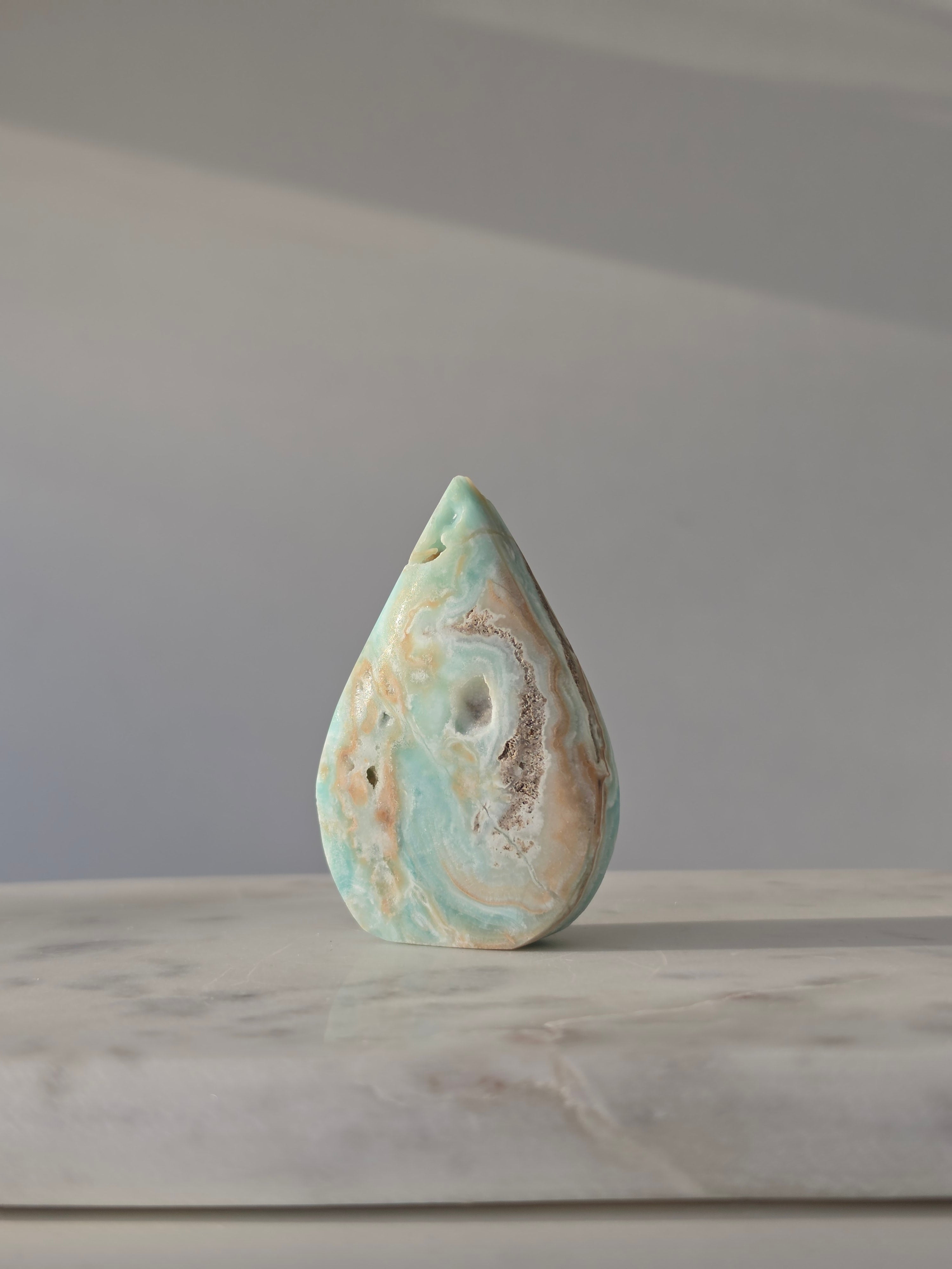 High-grade Hemimorphite flame featuring oceanic aqua and seafoam green banding, natural sculptural cavities, and flowing mineral patterns, photographed in natural light and curated by Stone and Bloom.
