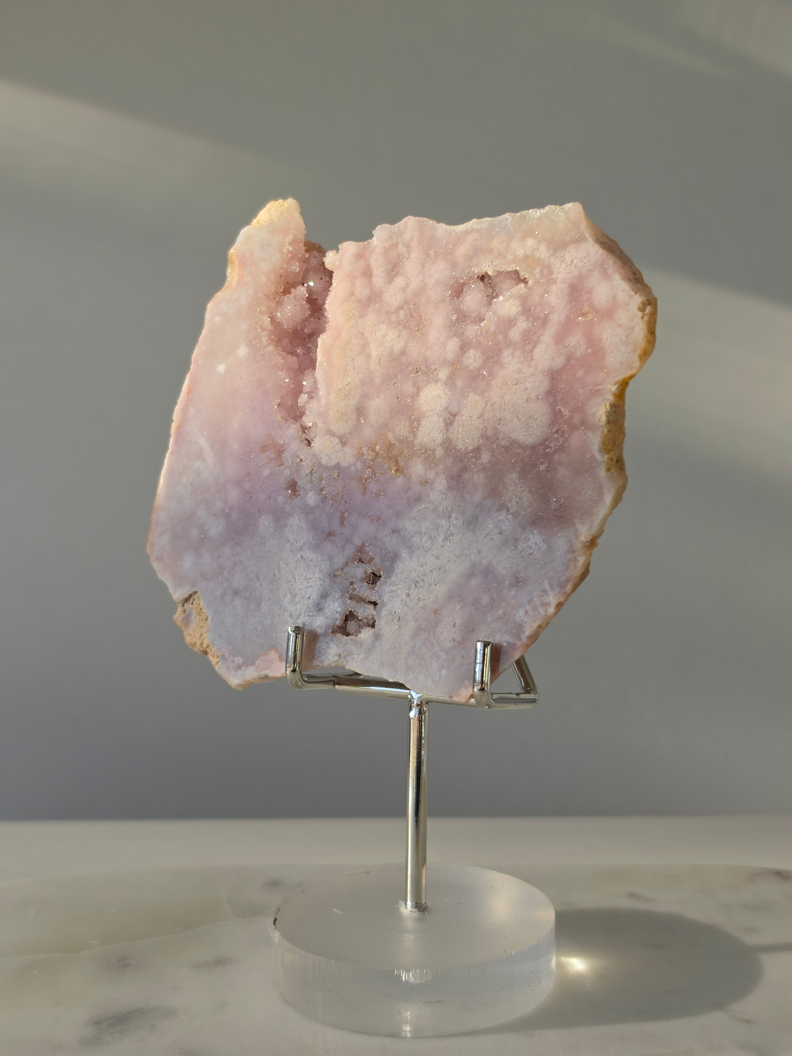 High-grade Pink Amethyst specimen on display stand featuring vibrant blush pink tones, sparkling druzy crystal formations, and natural crystalline pockets, curated by Stone and Bloom.