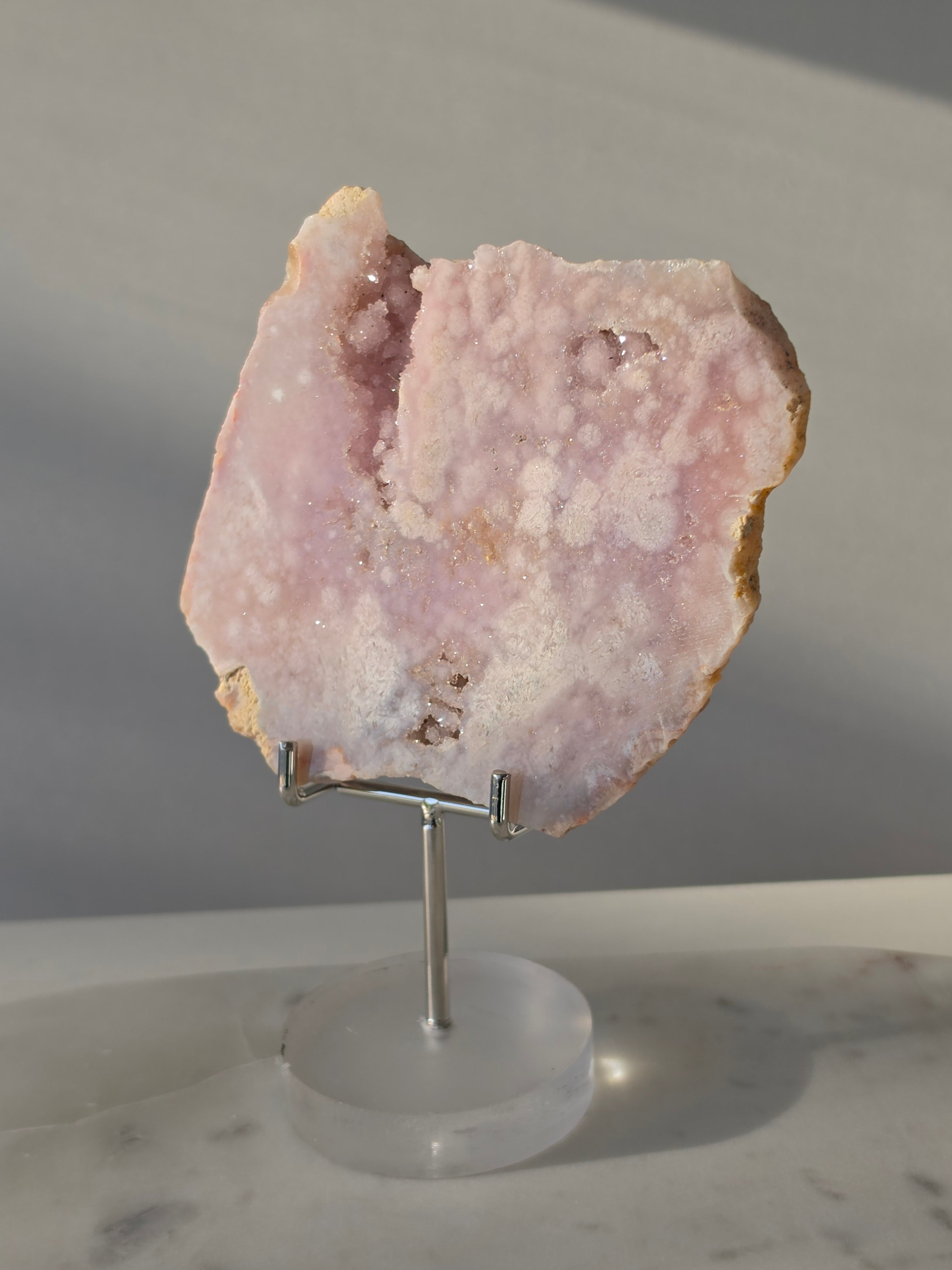 High-grade Pink Amethyst specimen on display stand featuring vibrant blush pink tones, sparkling druzy crystal formations, and natural crystalline pockets, curated by Stone and Bloom.