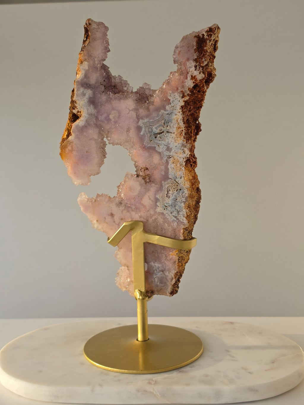 High-grade Brazilian Pink Amethyst slice on a gold display stand featuring sparkling blush-pink druzy crystals, natural agate banding, sculptural open formations, and delicate rose and champagne tones, photographed in natural light