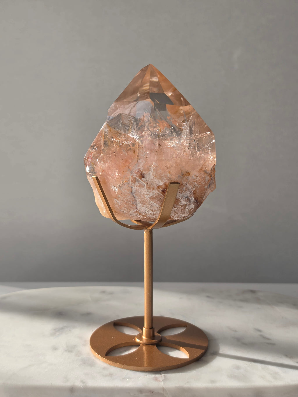 High-grade Nepalese Pink Himalayan Quartz statement piece, 697g and 19cm tall, featuring warm peachy-pink tones, translucent crystal formations and natural inclusions, displayed on a gold stand.