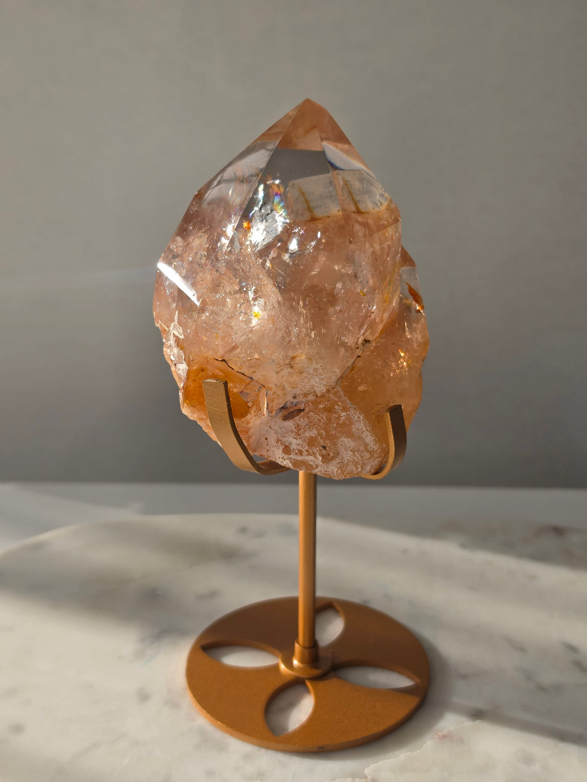 High-grade Nepalese Pink Himalayan Quartz statement piece, 697g and 19cm tall, featuring warm peachy-pink tones, translucent crystal formations and natural inclusions, displayed on a gold stand.