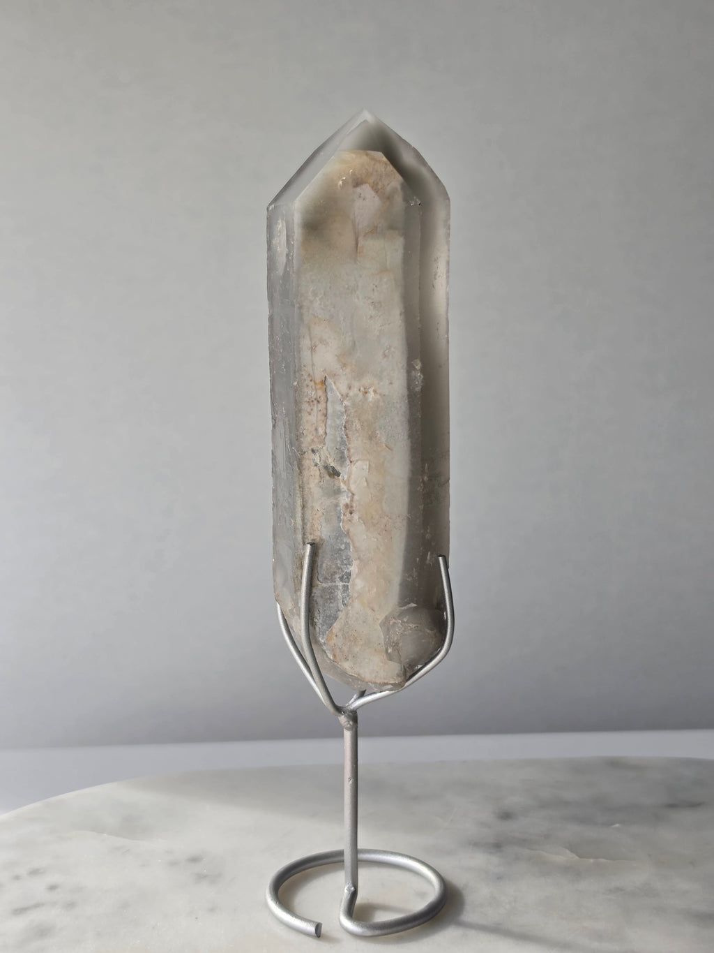 Translucent grey lithium crystal point with delicate internal phantom-like inclusions displayed on a silver-toned metal stand, 337g and approximately 20cm high.