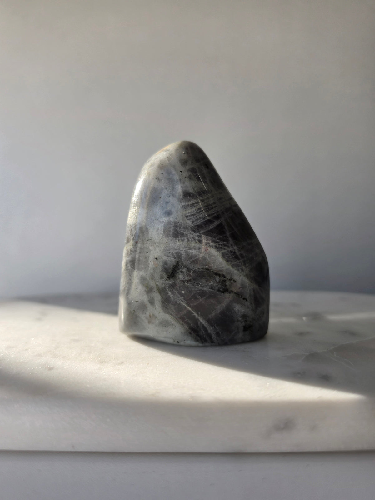 259g polished Labradorite cut base with smoky grey and charcoal colouring, natural silvery patterns and blue turquoise iridescence on the front.