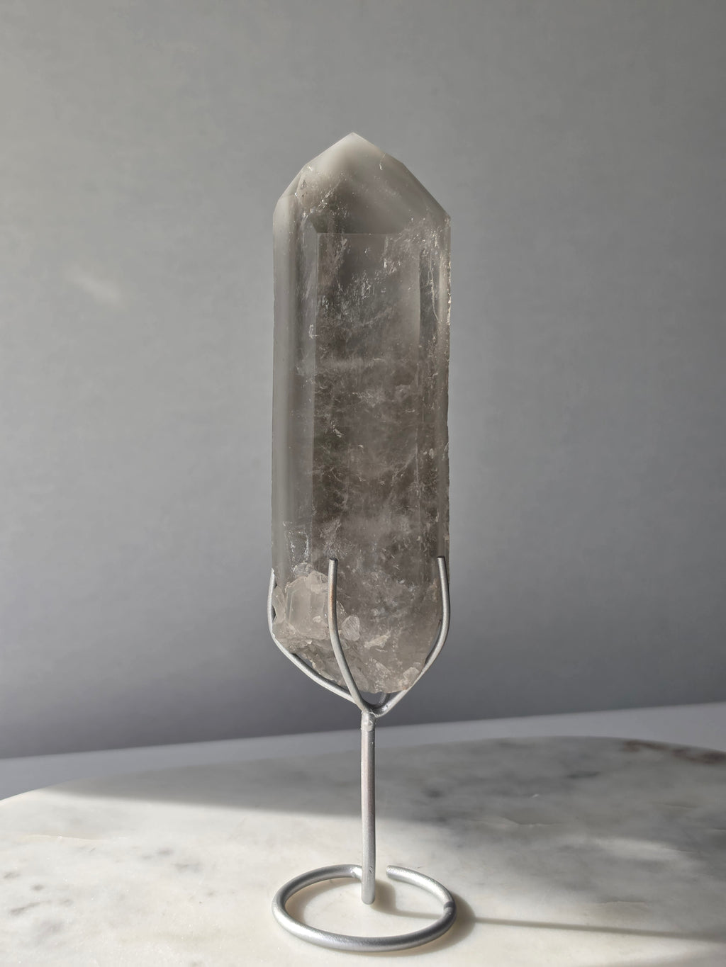 Translucent grey lithium crystal point with delicate internal phantom-like inclusions displayed on a silver-toned metal stand, 337g and approximately 20cm high.