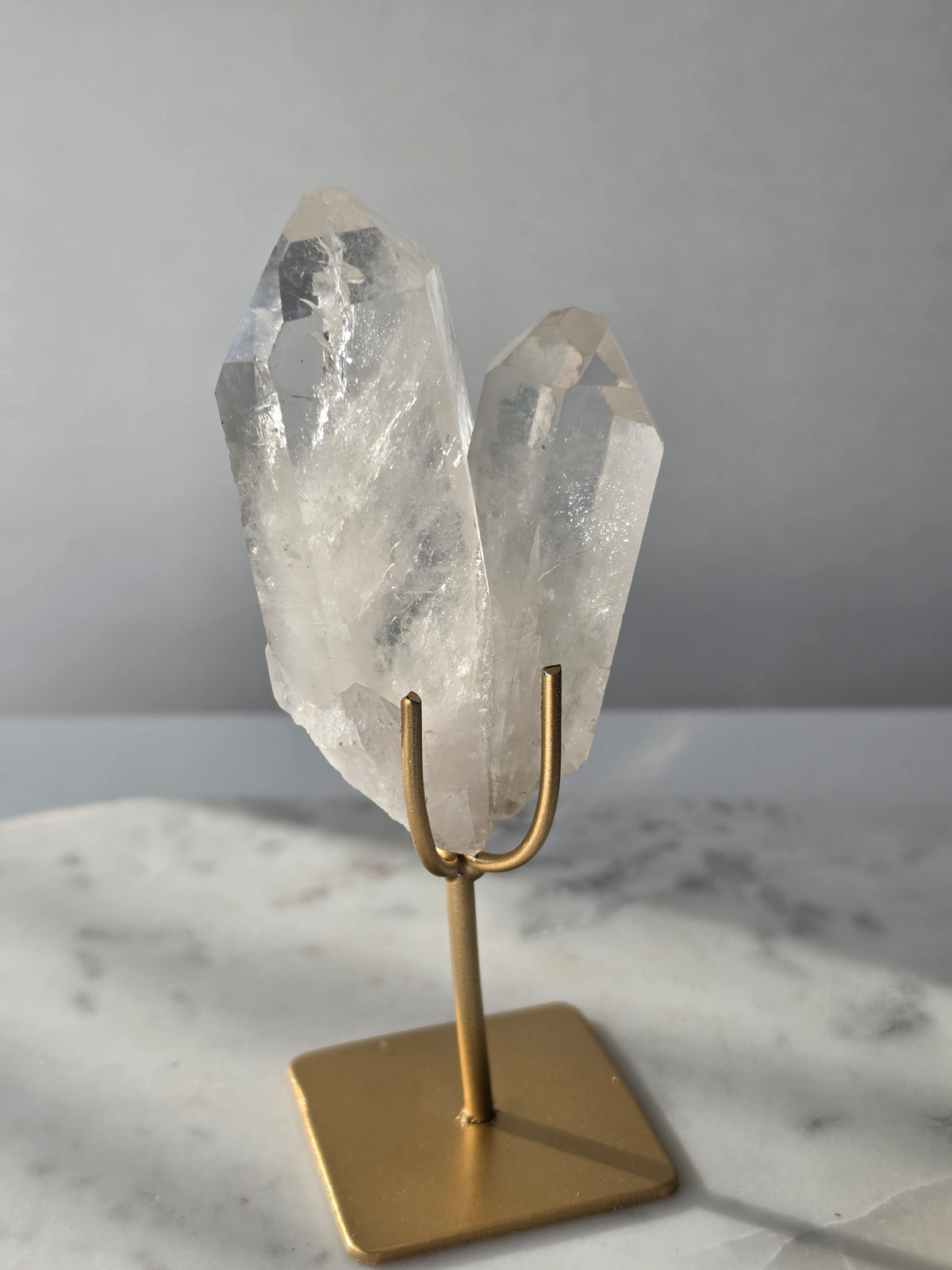 Clear Quartz Lemurian crystal on gold stand featuring exceptional clarity, natural rainbow inclusions, internal formations and striking crystal points