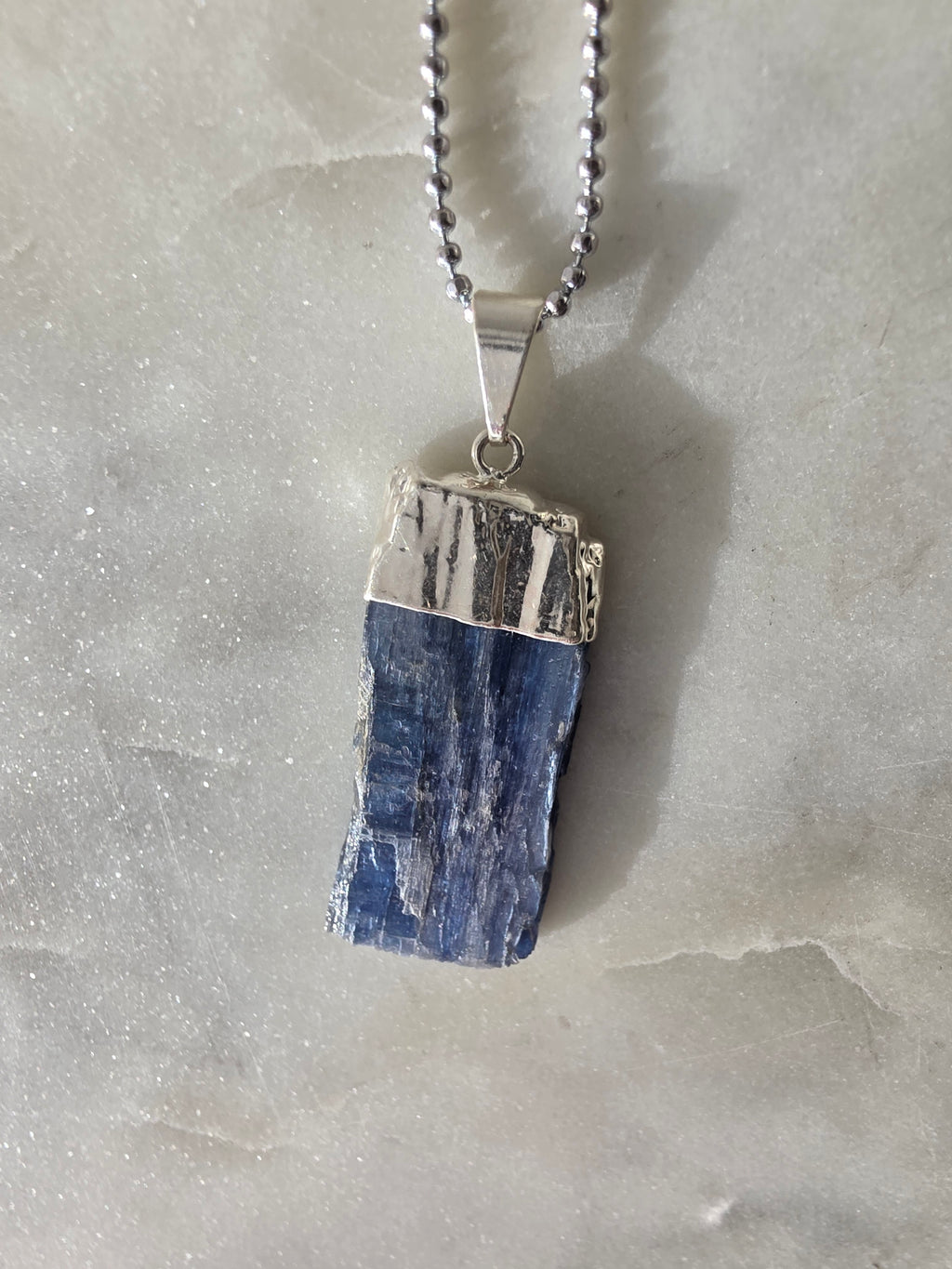 Natural Blue Kyanite raw crystal pendant with silver-plated cap from the Stone & Bloom Raw Luxe Collection, featuring deep blue tones and natural crystal texture.