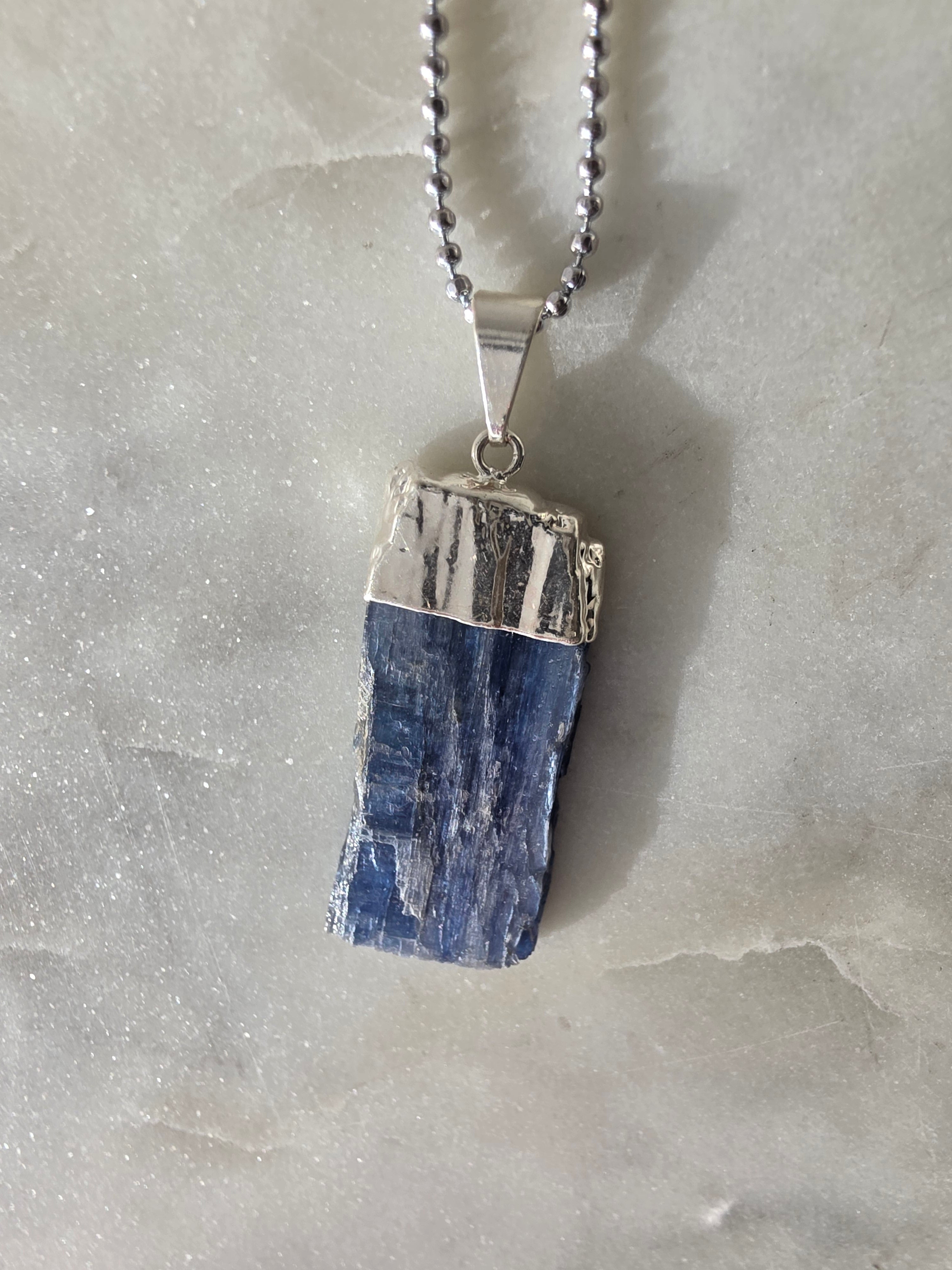 Natural Blue Kyanite raw crystal pendant with silver-plated cap from the Stone & Bloom Raw Luxe Collection, featuring deep blue tones and natural crystal texture.