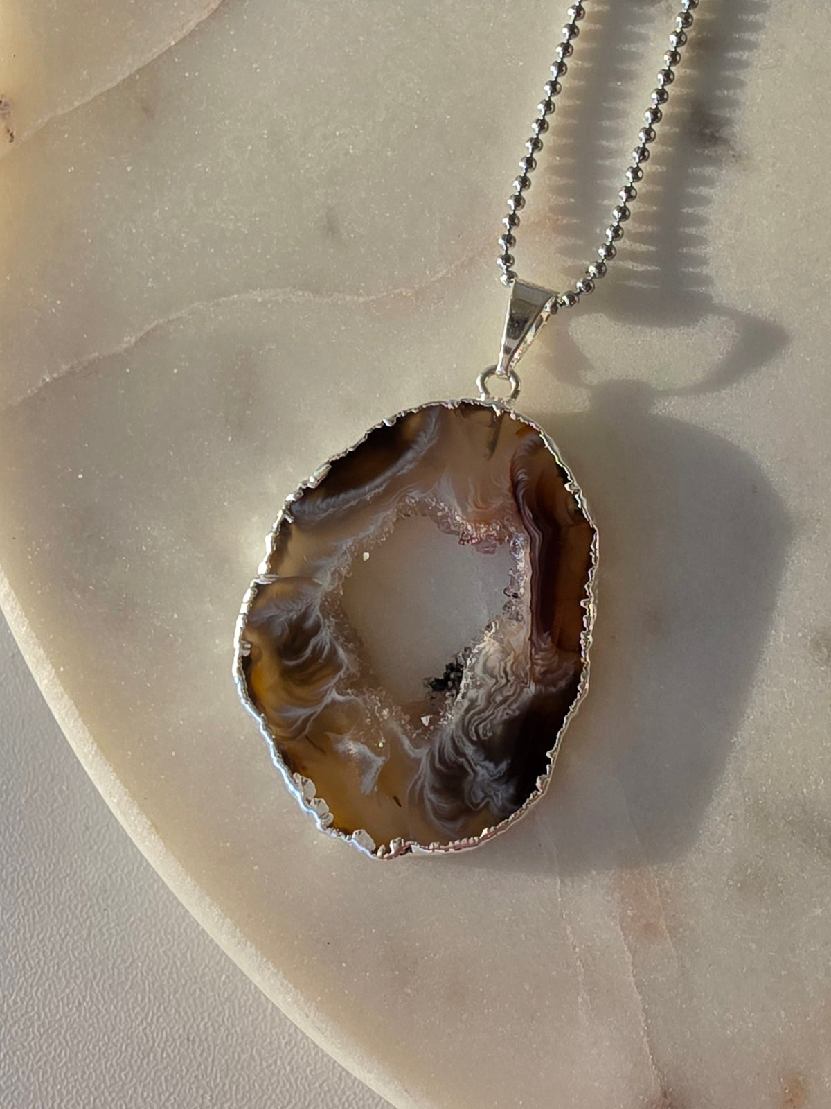 "Brazilian Agate Geode Slice Pendant in natural [brown/black/grey] tones on a silver plated chain with sparkling druzy crystal formations"