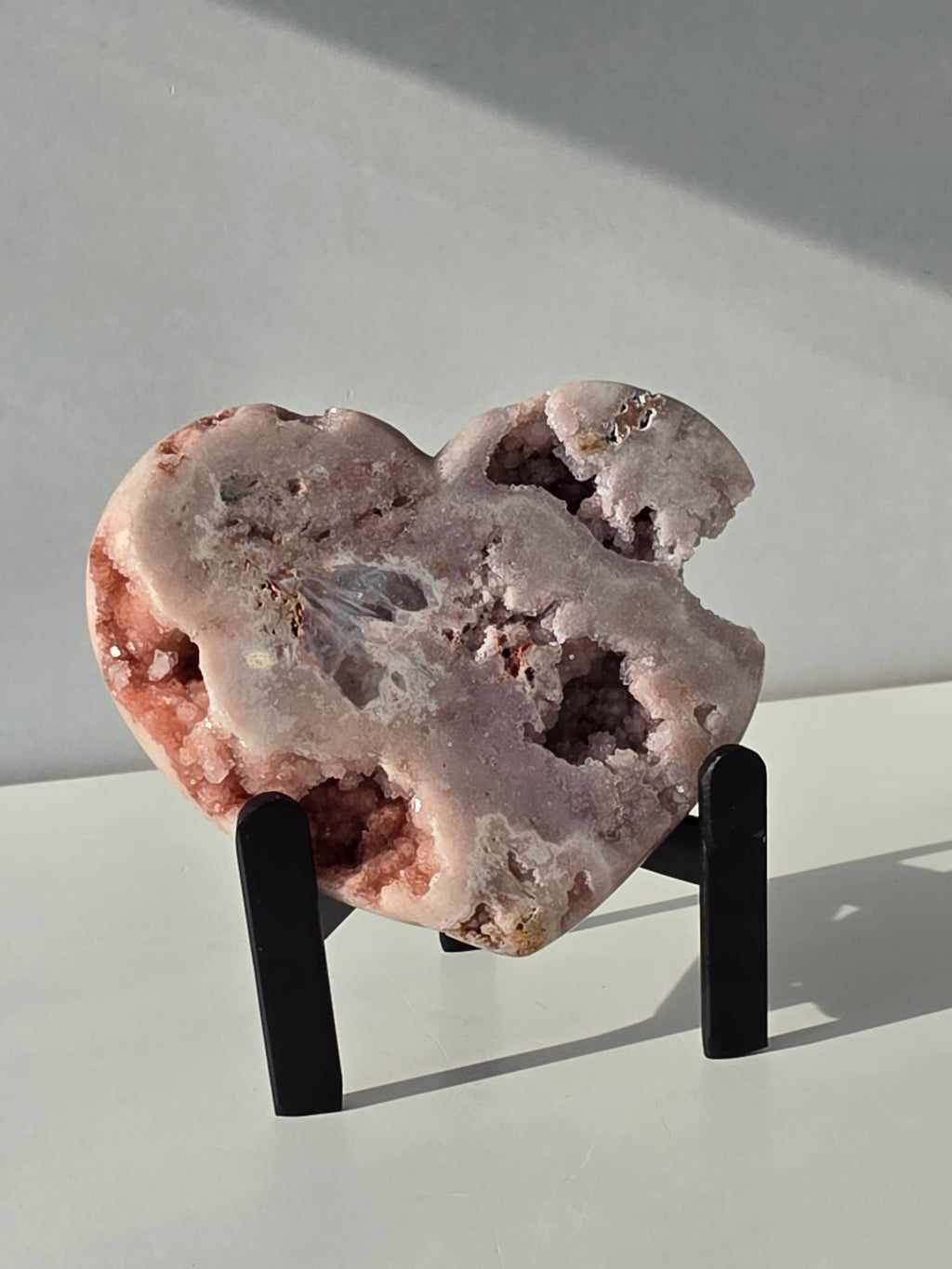 Brazilian Pink Amethyst druzy heart crystal on black metal stand with natural crystal caves and blush pink quartz, luxury crystal décor by Stone & Bloom