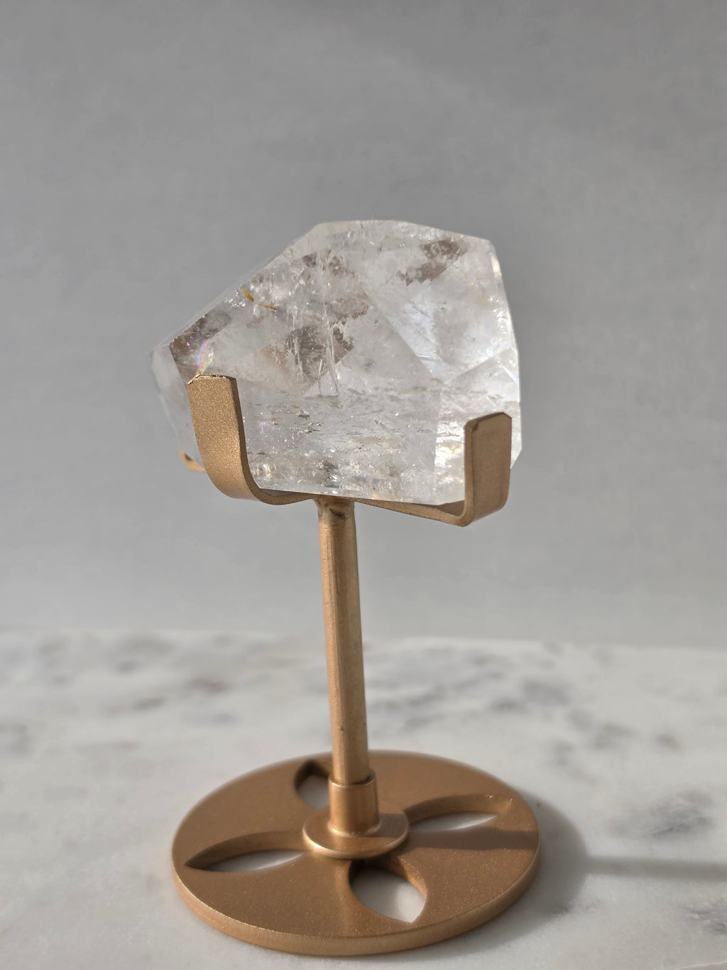 Clear Quartz freeform crystal with natural internal inclusions and luminous clarity, displayed on an elegant gold-finished stand.