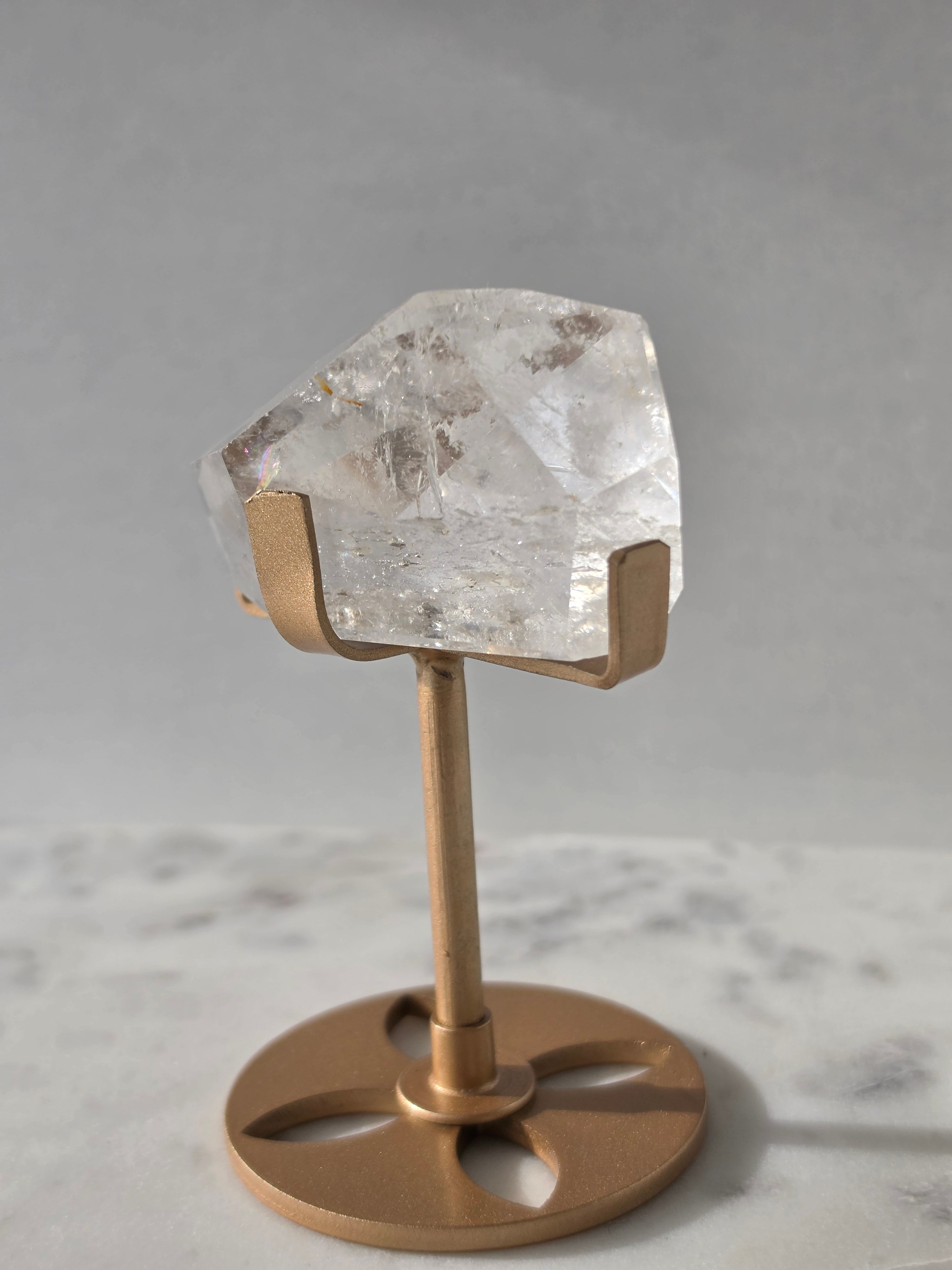 Clear Quartz freeform crystal with natural internal inclusions and luminous clarity, displayed on an elegant gold-finished stand.