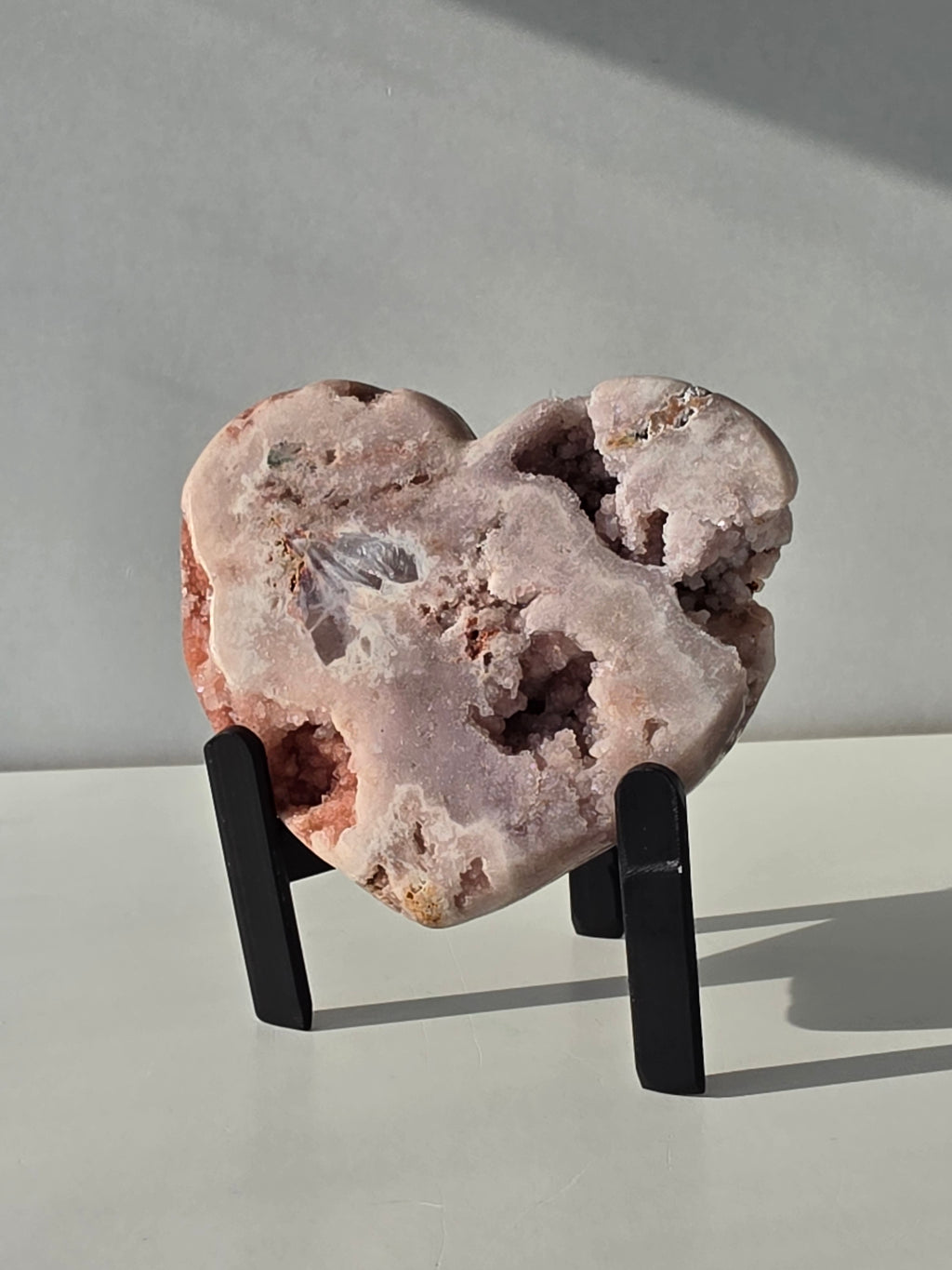 Brazilian Pink Amethyst druzy heart crystal on black metal stand with natural crystal caves and blush pink quartz, luxury crystal décor by Stone & Bloom