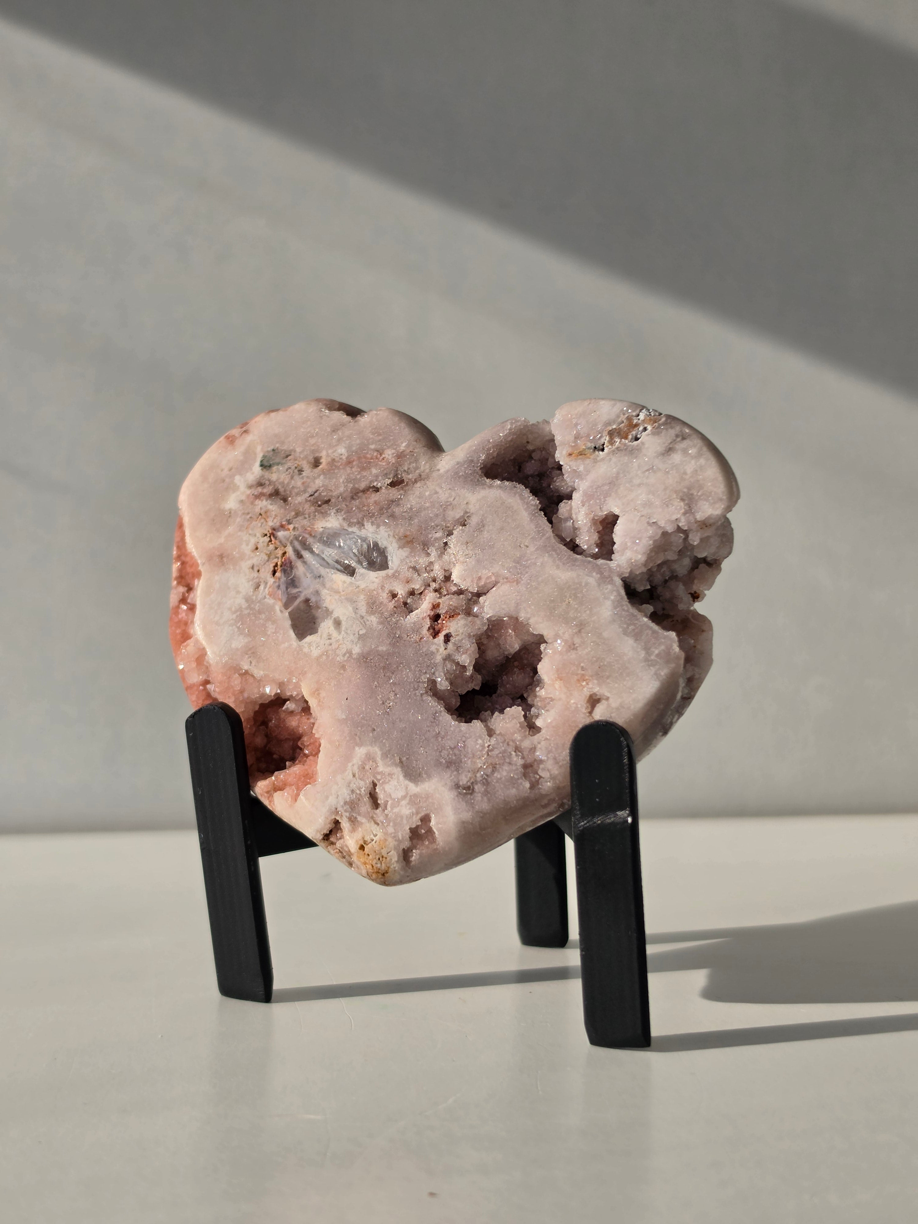 Brazilian Pink Amethyst druzy heart crystal on black metal stand with natural crystal caves and blush pink quartz, luxury crystal décor by Stone & Bloom