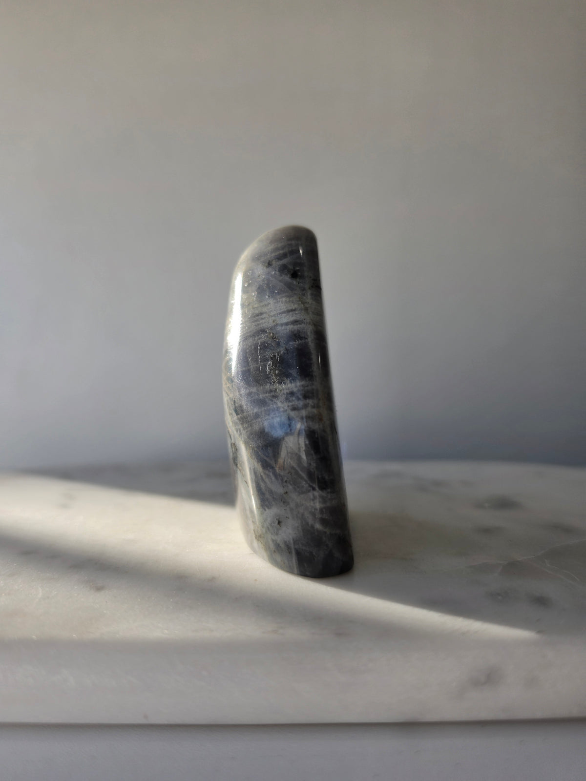 259g polished Labradorite cut base with smoky grey and charcoal colouring, natural silvery patterns and blue turquoise iridescence on the front.