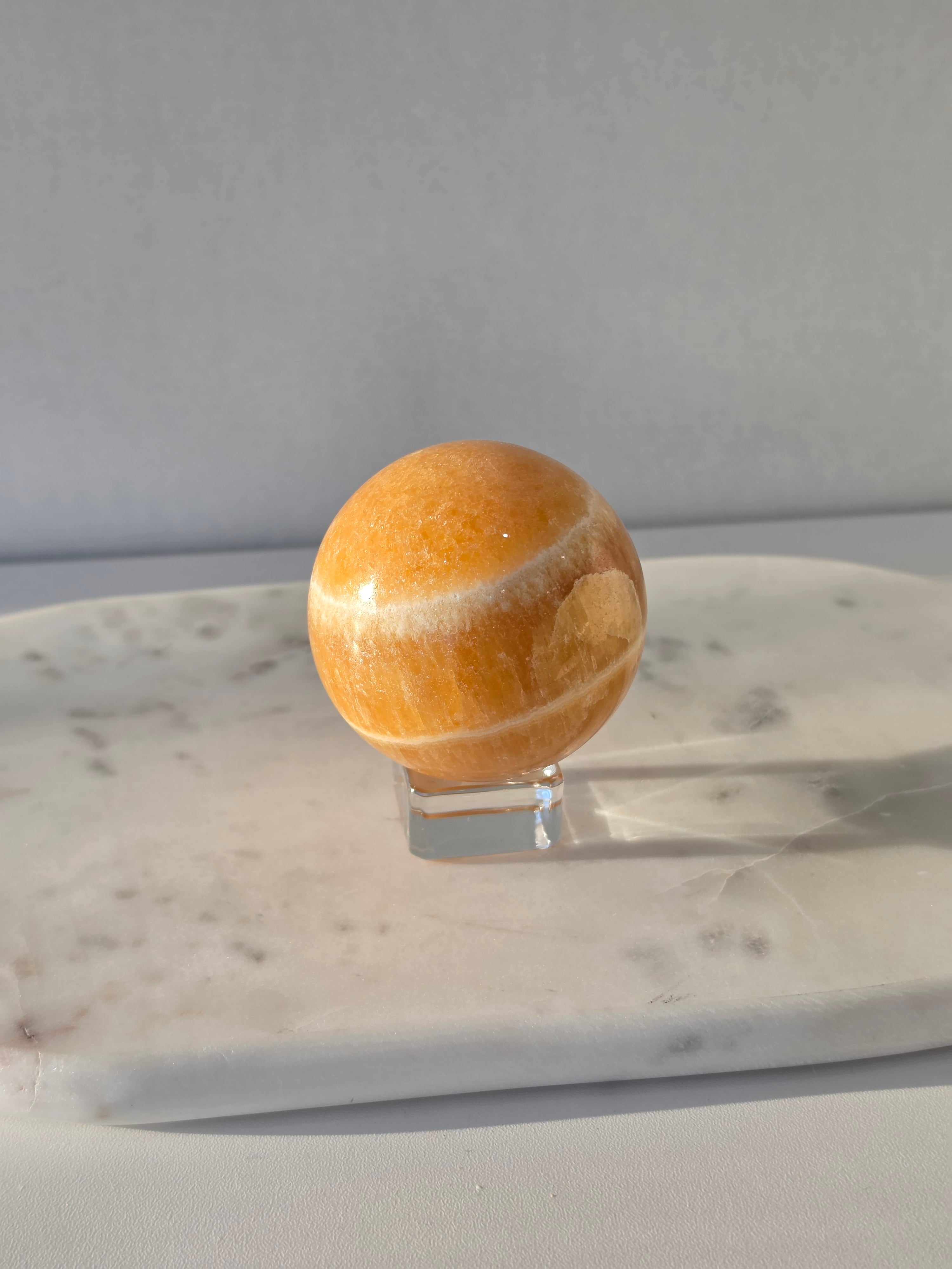 Natural Orange Calcite Sphere with warm golden-orange banding, polished to a high shine and hand-selected by Stone & Bloom.