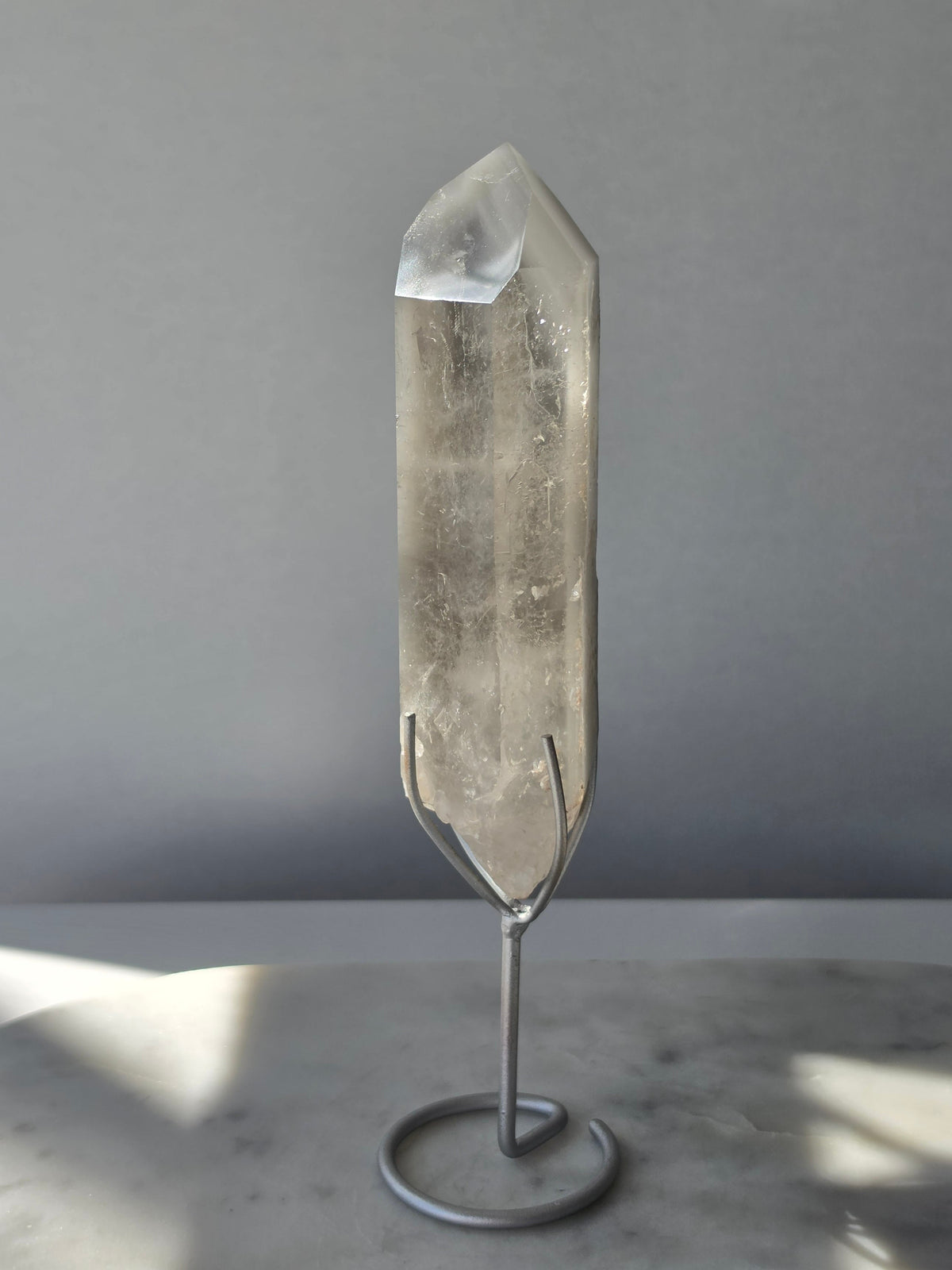 Translucent grey lithium crystal point with delicate internal phantom-like inclusions displayed on a silver-toned metal stand, 337g and approximately 20cm high.