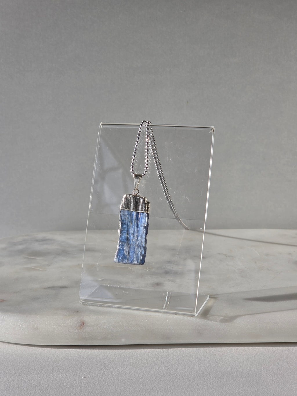 Natural Blue Kyanite raw crystal pendant with silver-plated cap from the Stone & Bloom Raw Luxe Collection, featuring deep blue tones and natural crystal texture.