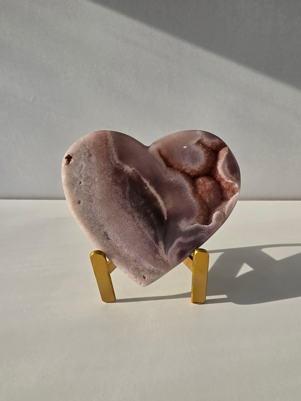 Natural Brazilian Pink Amethyst heart crystal on gold metal stand featuring blush pink banding and sparkling druzy quartz, luxury crystal home décor by Stone & Bloom.