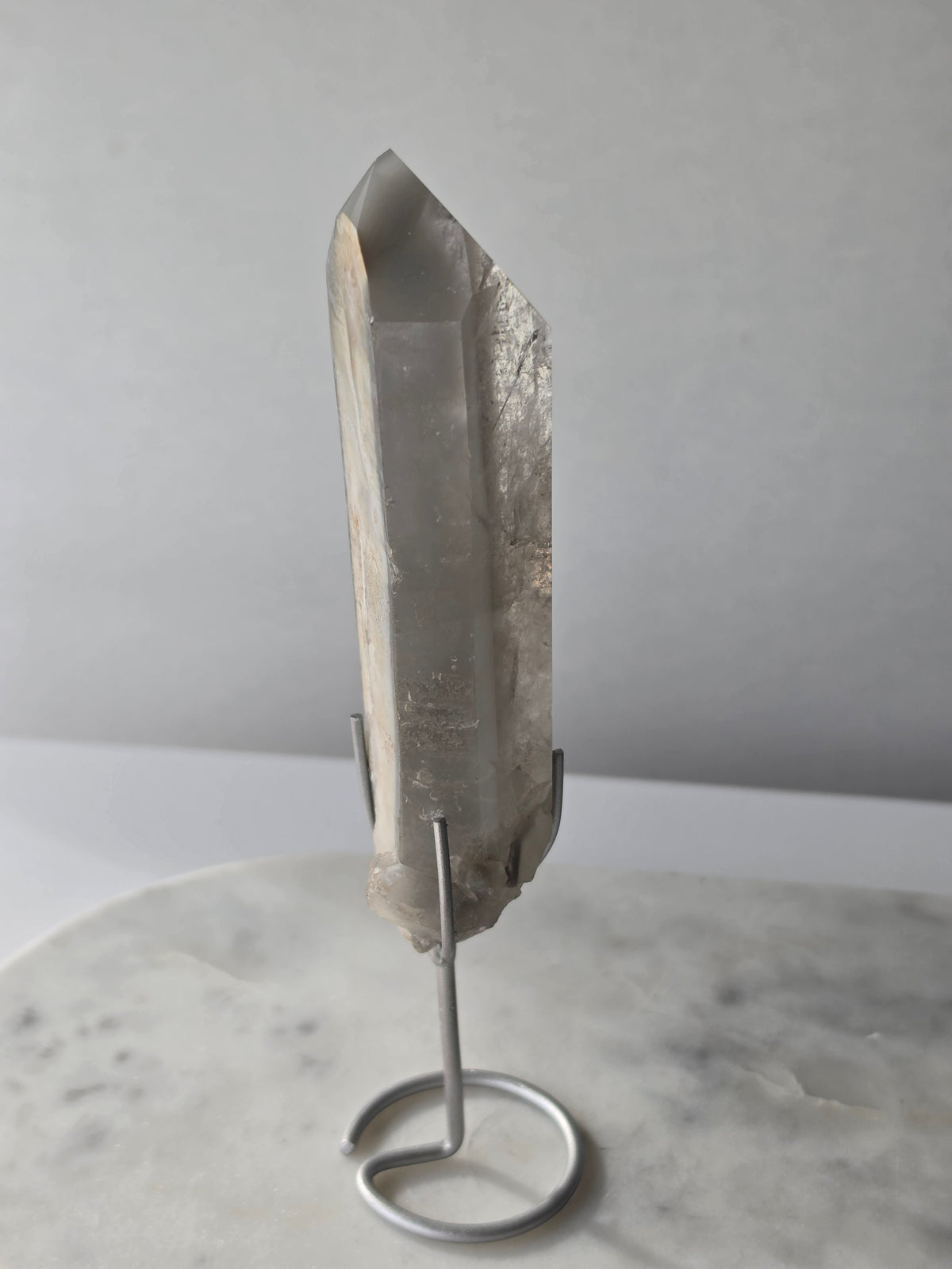 Translucent grey lithium crystal point with delicate internal phantom-like inclusions displayed on a silver-toned metal stand, 337g and approximately 20cm high.
