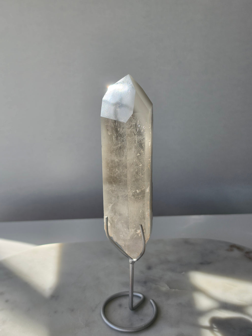 Translucent grey lithium crystal point with delicate internal phantom-like inclusions displayed on a silver-toned metal stand, 337g and approximately 20cm high.