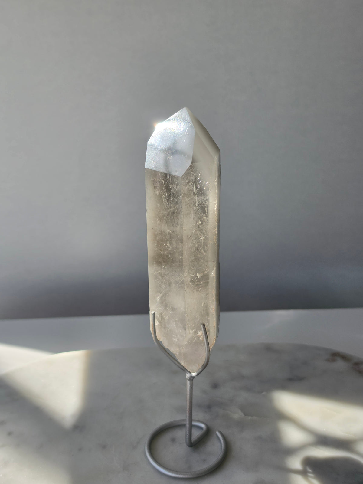 Translucent grey lithium crystal point with delicate internal phantom-like inclusions displayed on a silver-toned metal stand, 337g and approximately 20cm high.