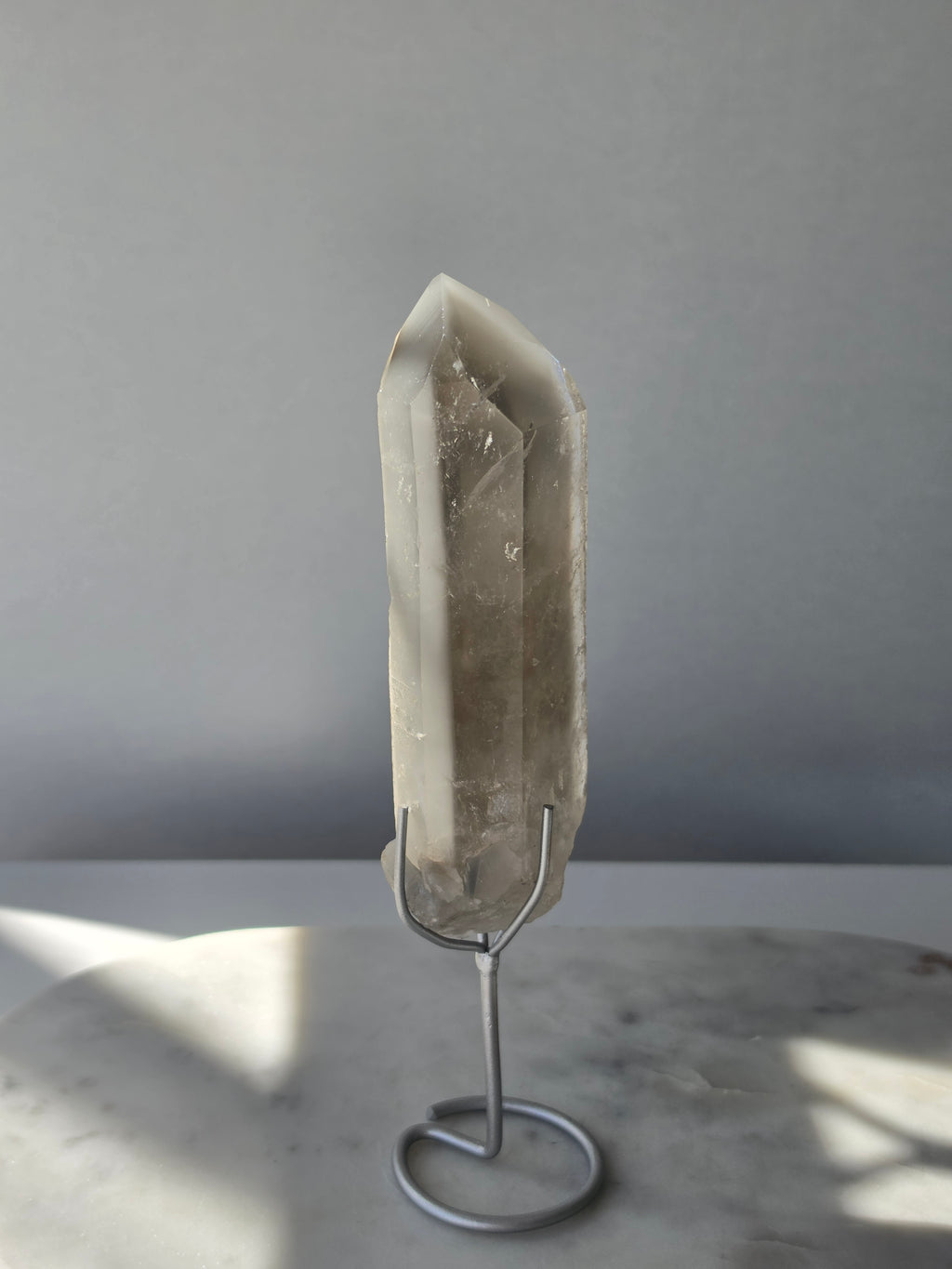 Translucent grey lithium crystal point with delicate internal phantom-like inclusions displayed on a silver-toned metal stand, 337g and approximately 20cm high.