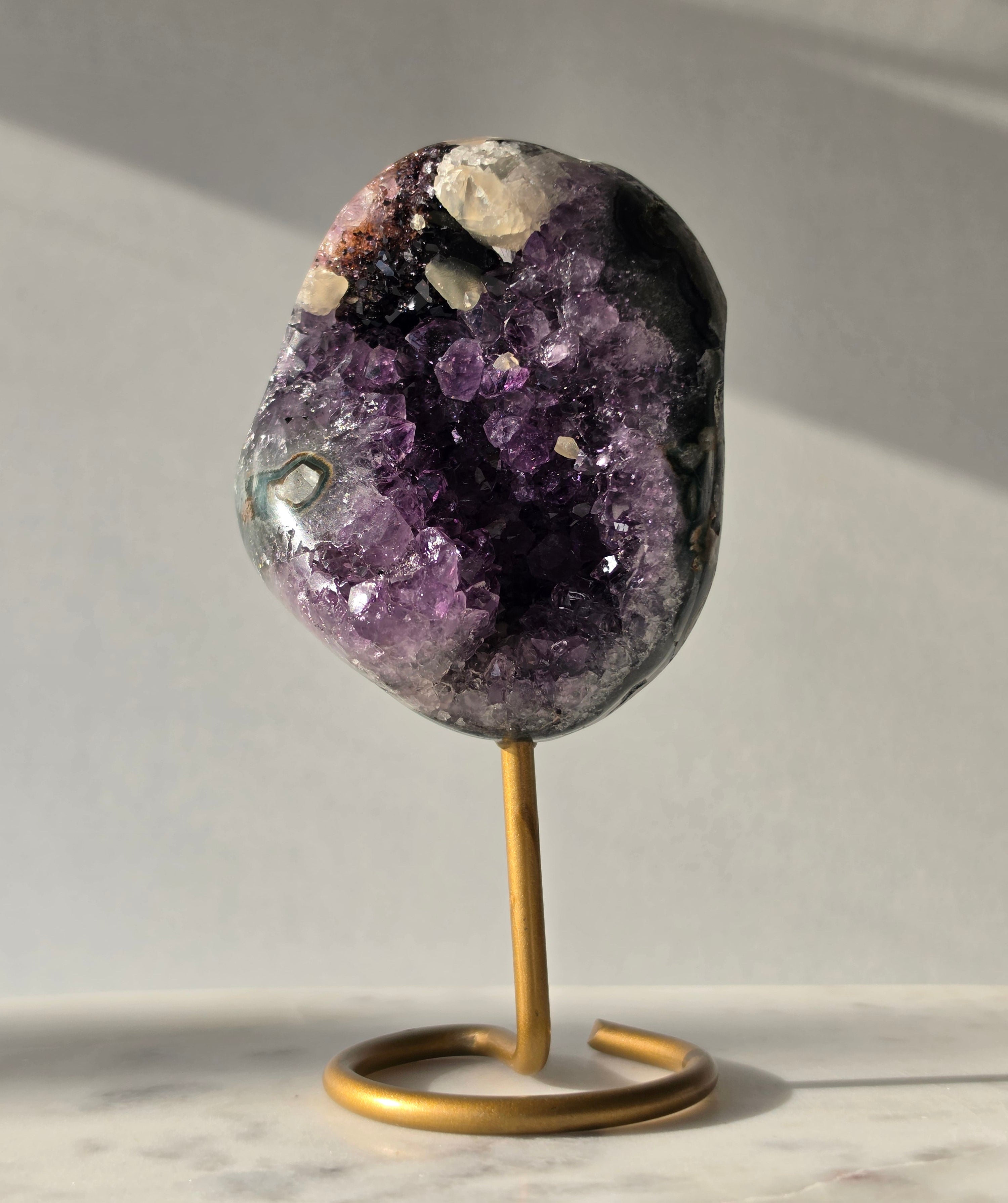 Natural Amethyst Stalactite with Calcite inclusions and blush red tones on a luxury gold display stand