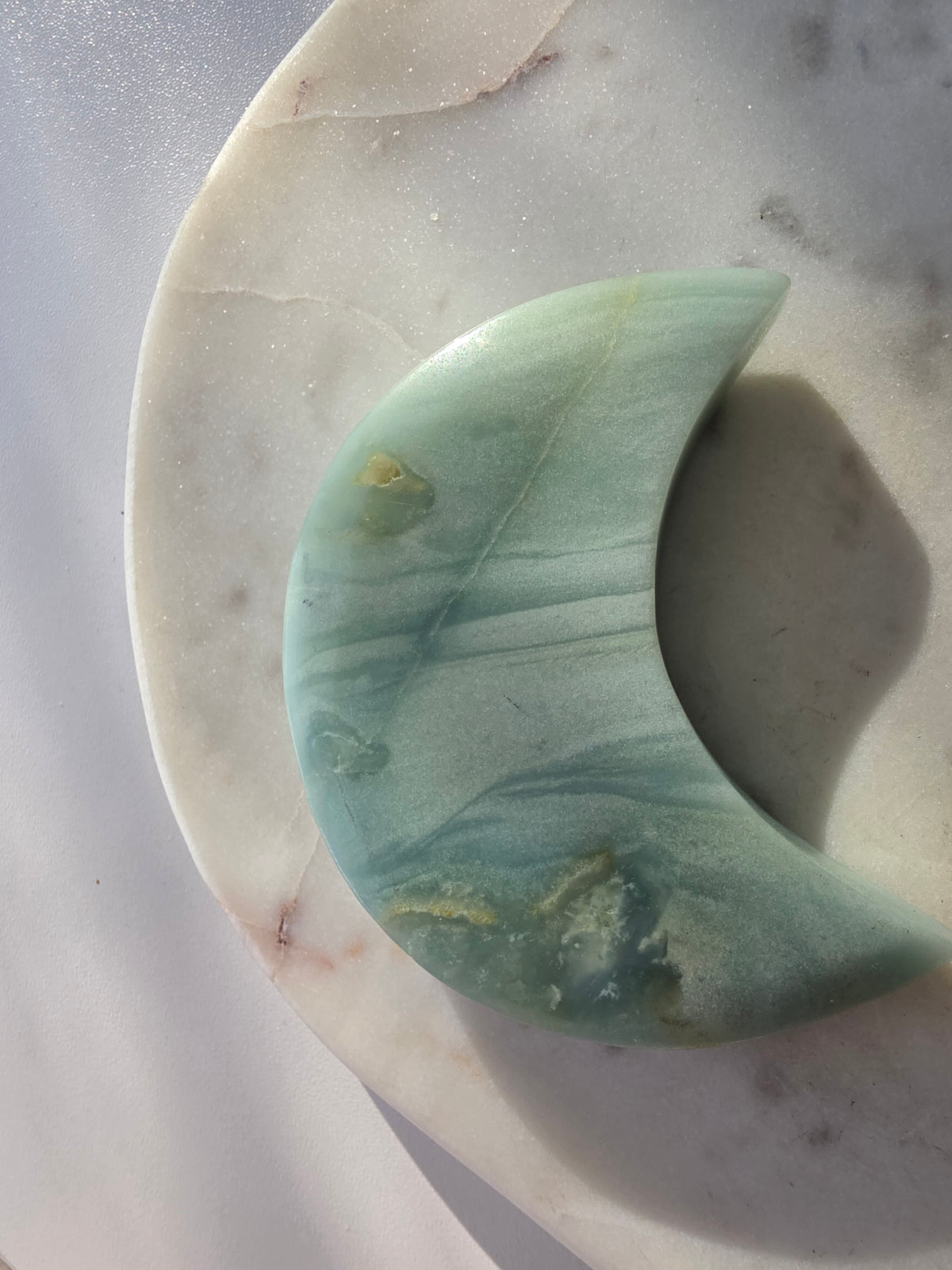 Natural Amazonite crescent moon with soft seafoam green and blue-green banding, subtle golden-brown inclusions and polished finish, displayed on a silver stand.