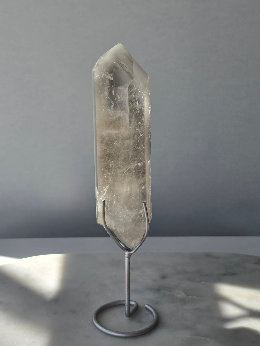 Translucent grey lithium crystal point with delicate internal phantom-like inclusions displayed on a silver-toned metal stand, 337g and approximately 20cm high.