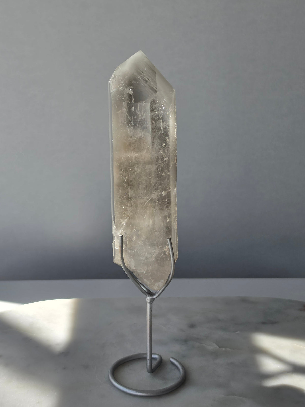 Translucent grey lithium crystal point with delicate internal phantom-like inclusions displayed on a silver-toned metal stand, 337g and approximately 20cm high.