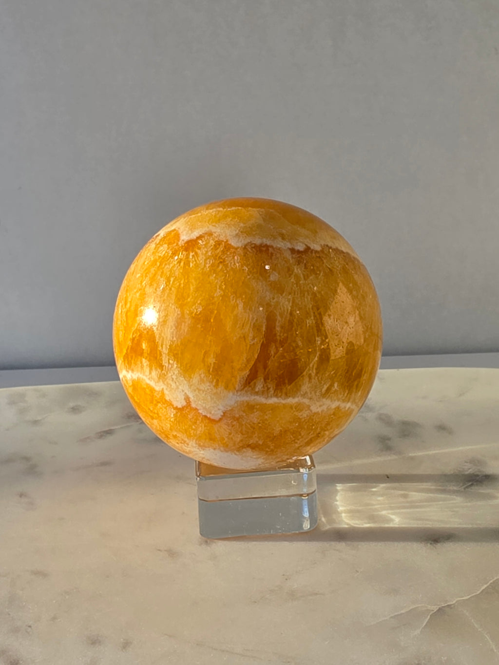 Natural Orange Calcite Sphere with warm golden-orange banding, polished to a high shine and hand-selected by Stone & Bloom.