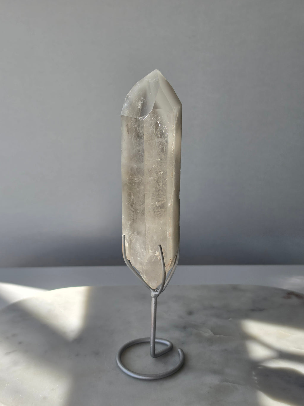 Translucent grey lithium crystal point with delicate internal phantom-like inclusions displayed on a silver-toned metal stand, 337g and approximately 20cm high.
