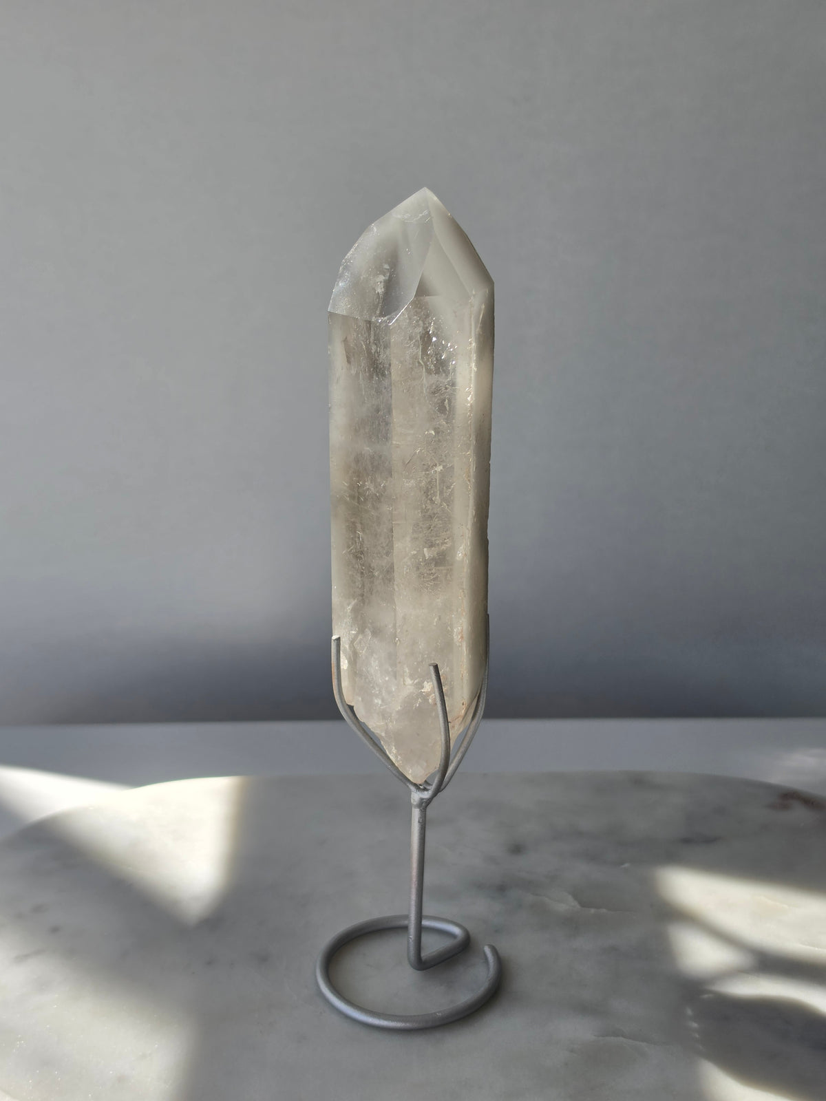 Translucent grey lithium crystal point with delicate internal phantom-like inclusions displayed on a silver-toned metal stand, 337g and approximately 20cm high.