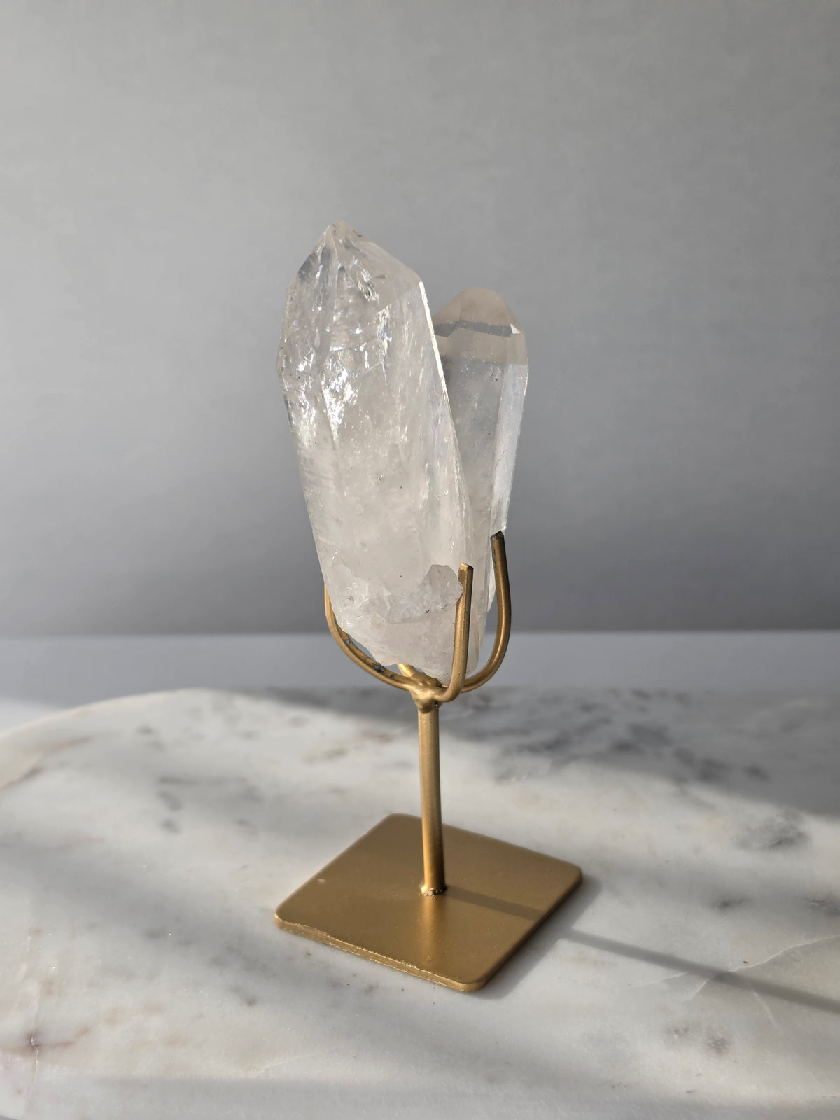 Clear Quartz Lemurian crystal on gold stand featuring exceptional clarity, natural rainbow inclusions, internal formations and striking crystal points