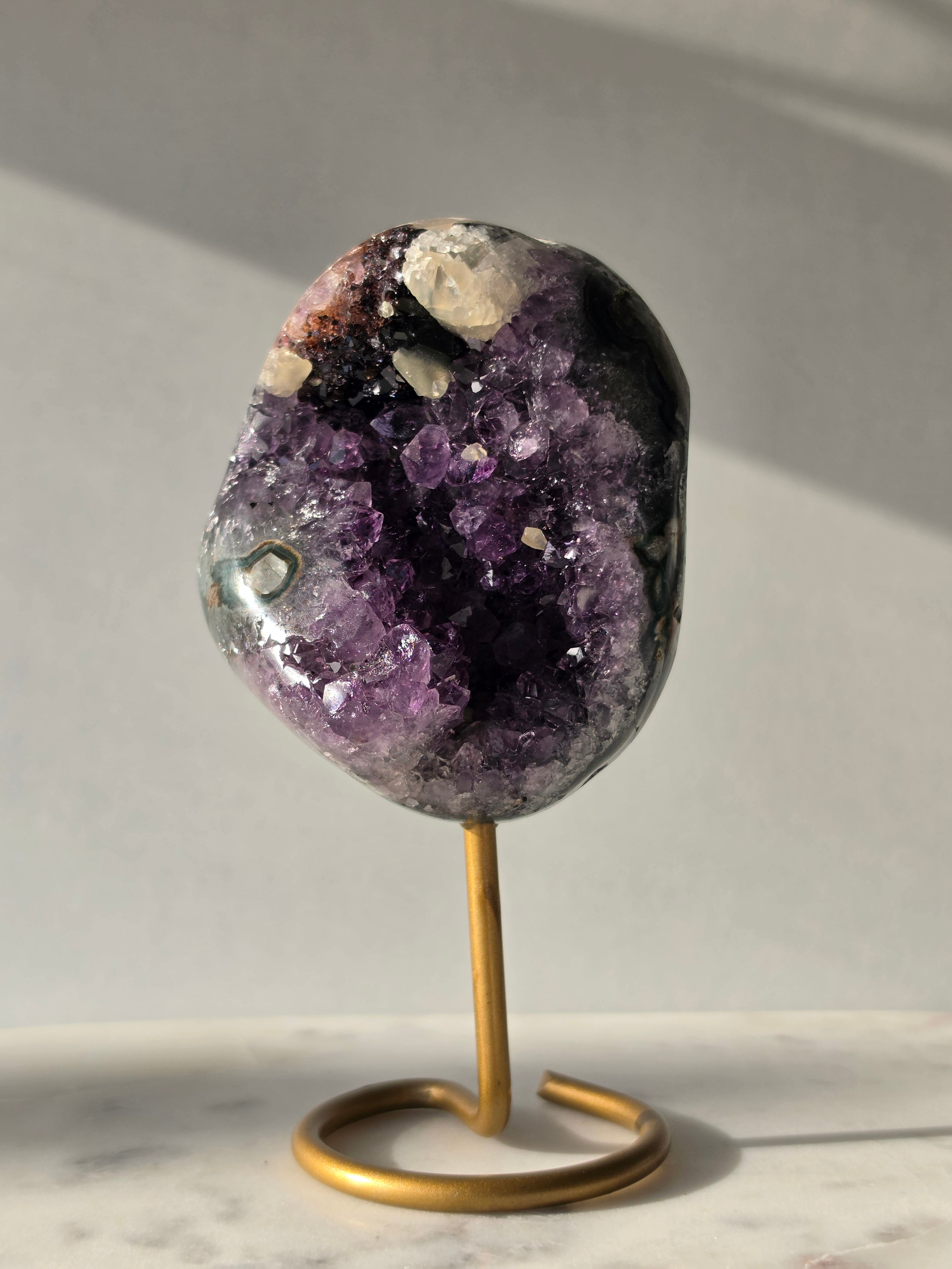 Natural Amethyst Stalactite with Calcite inclusions and blush red tones on a luxury gold display stand