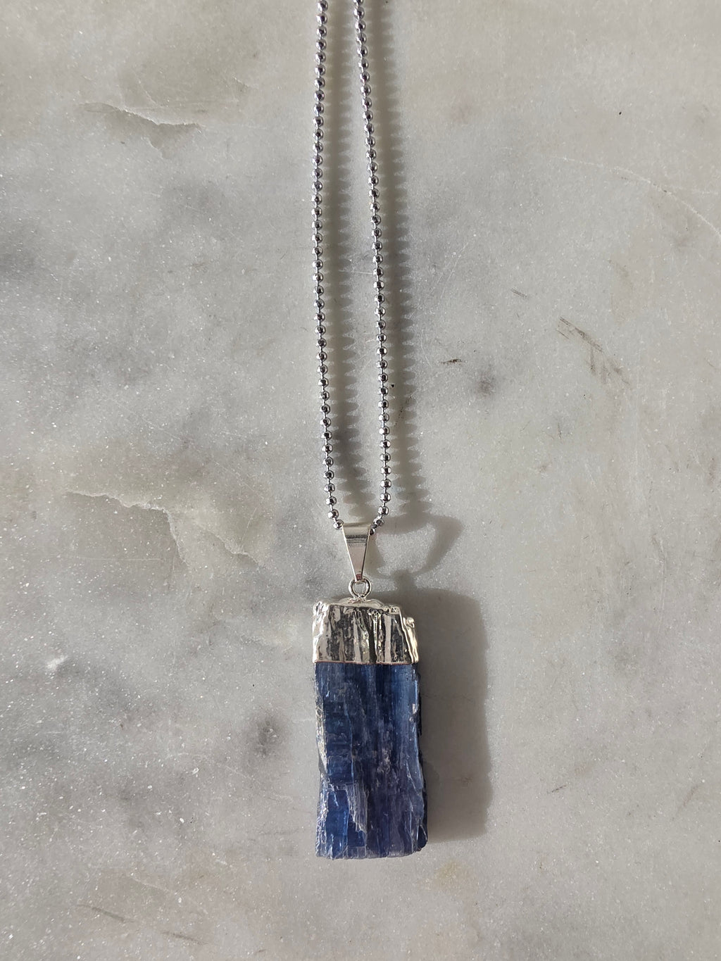 Natural Blue Kyanite raw crystal pendant with silver-plated cap from the Stone & Bloom Raw Luxe Collection, featuring deep blue tones and natural crystal texture.
