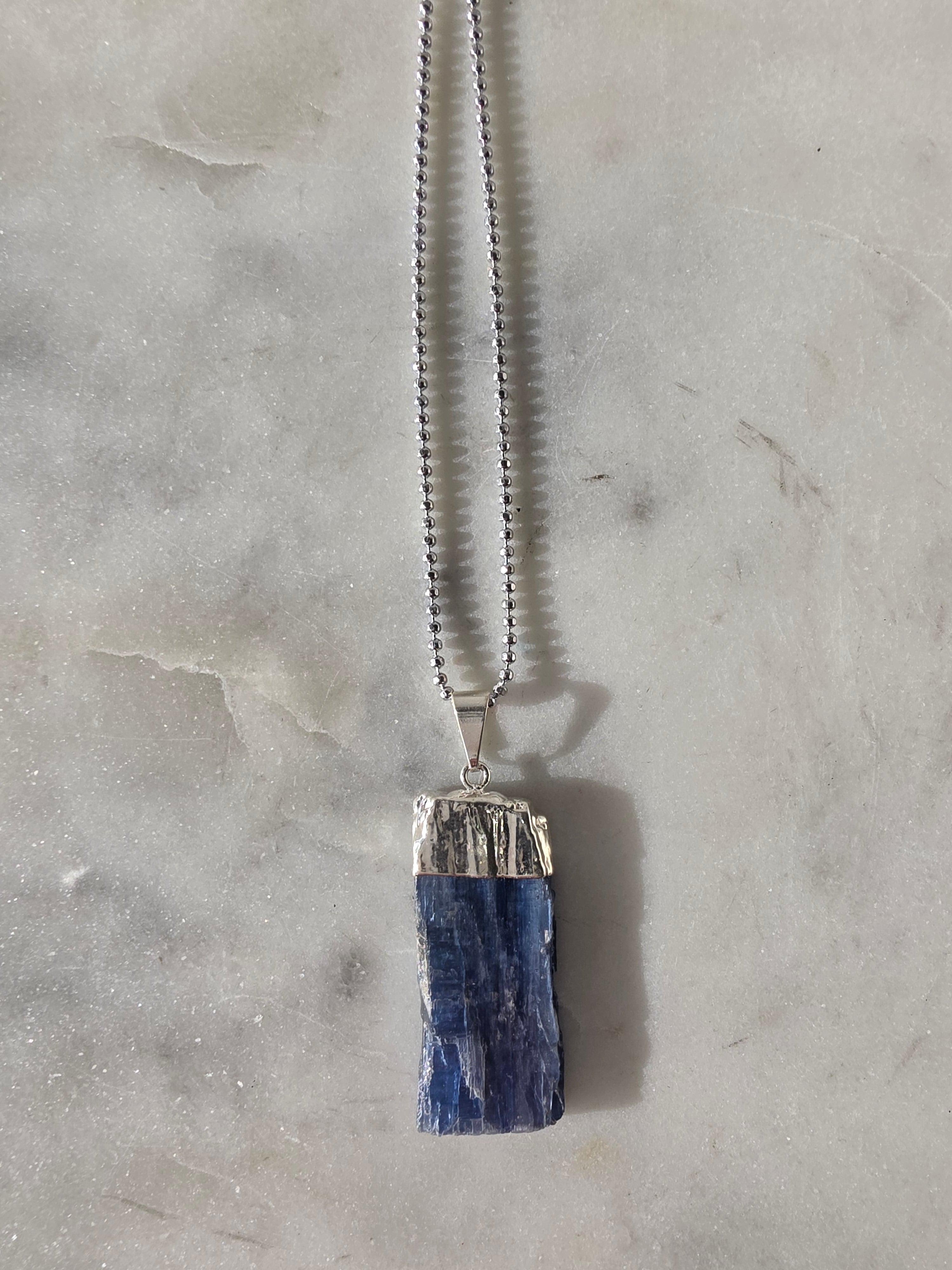 Natural Blue Kyanite raw crystal pendant with silver-plated cap from the Stone & Bloom Raw Luxe Collection, featuring deep blue tones and natural crystal texture.