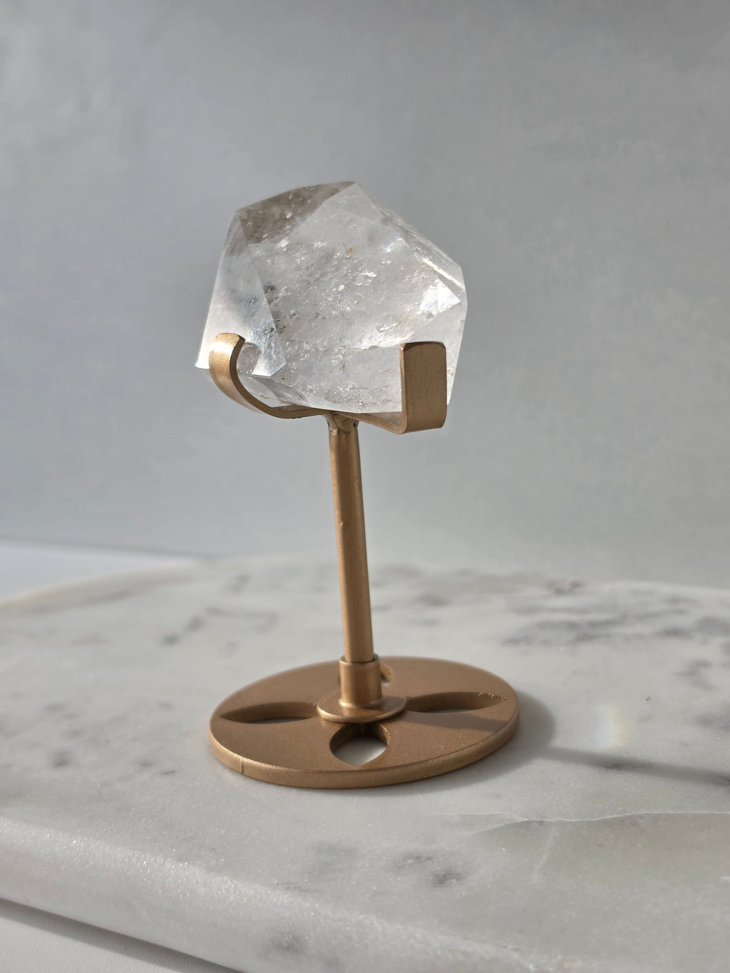 Clear Quartz freeform crystal with natural internal inclusions and luminous clarity, displayed on an elegant gold-finished stand.