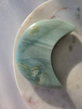 Natural Amazonite crescent moon with soft seafoam green and blue-green banding, subtle golden-brown inclusions and polished finish, displayed on a silver stand.