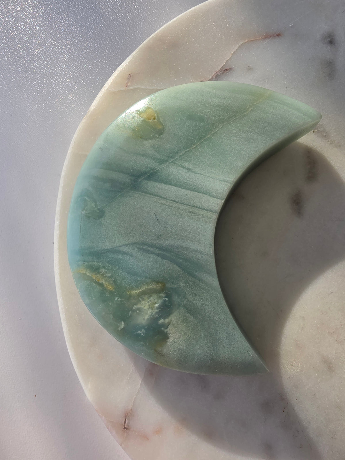 Natural Amazonite crescent moon with soft seafoam green and blue-green banding, subtle golden-brown inclusions and polished finish, displayed on a silver stand.